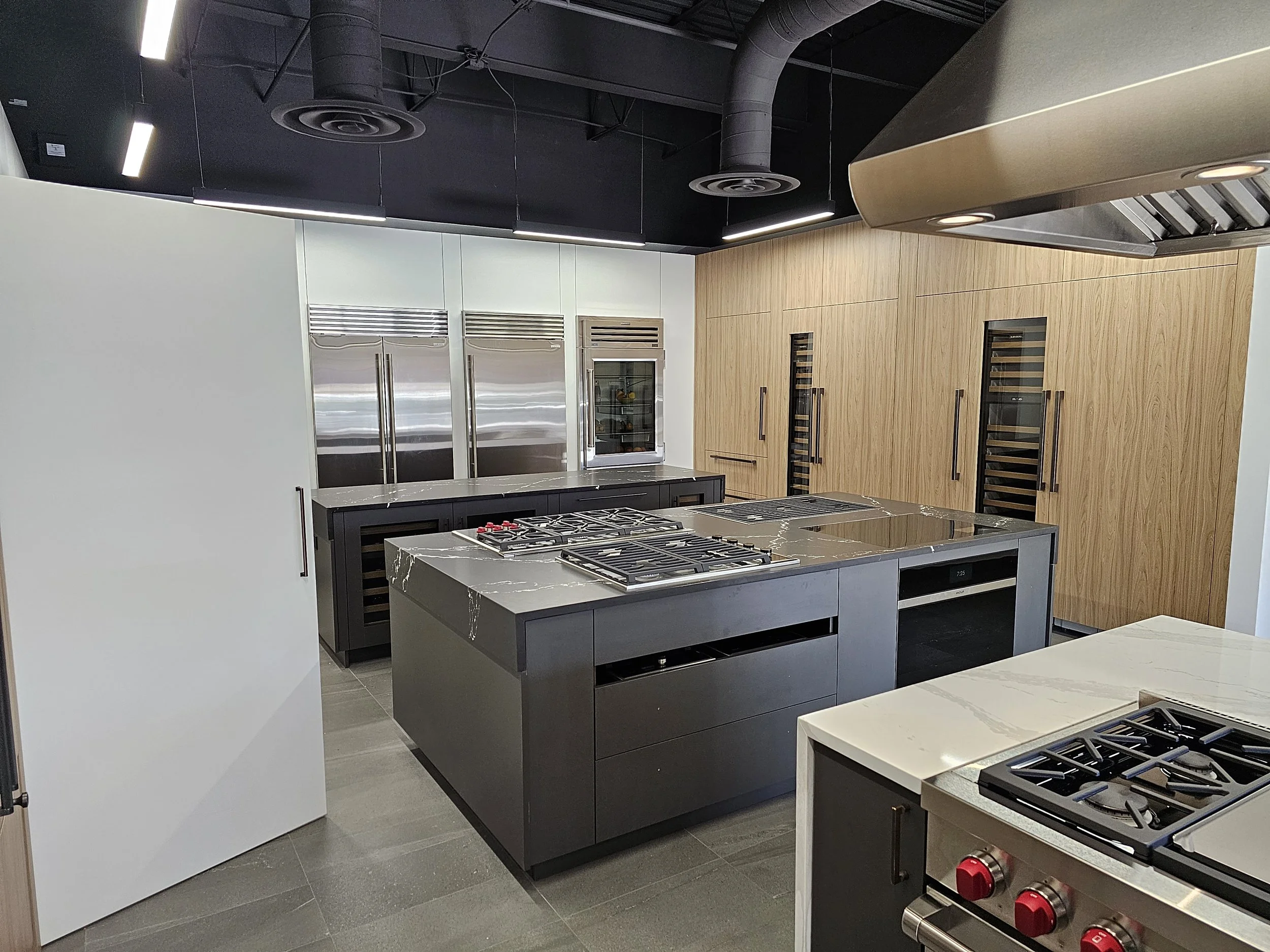 Modern kitchen with gray and wood cabinets, stainless steel appliances, and a black marble island stove.