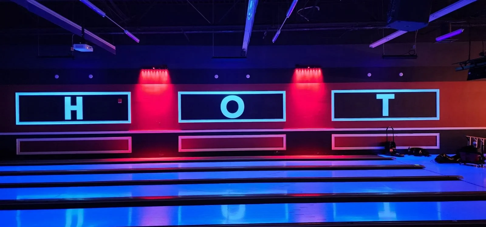 A neon-lit bowling alley with illuminated letters spelling 'H', 'O', and 'T' on the electronic score display boards.