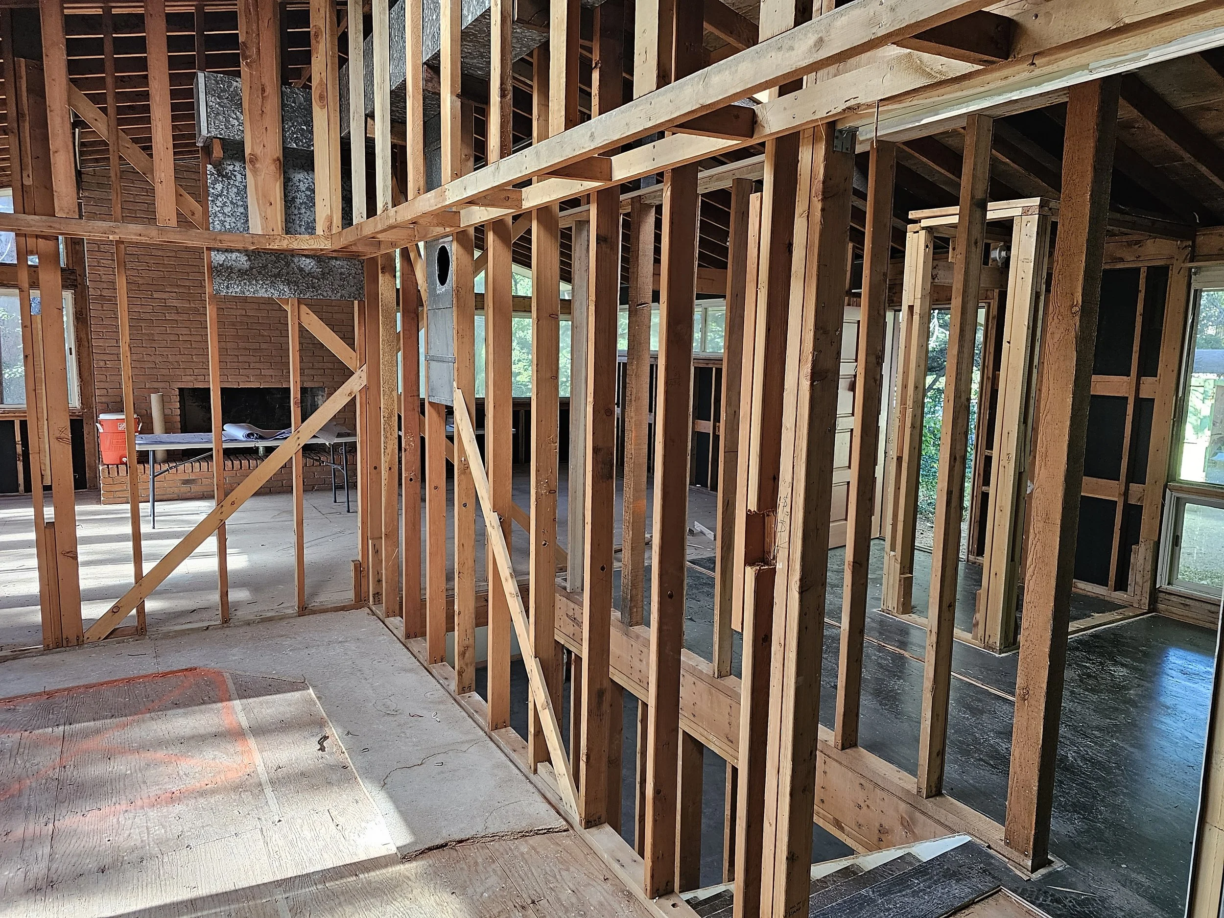Interior view of a house under construction showing exposed wooden framing, partial brick wall, and windows.