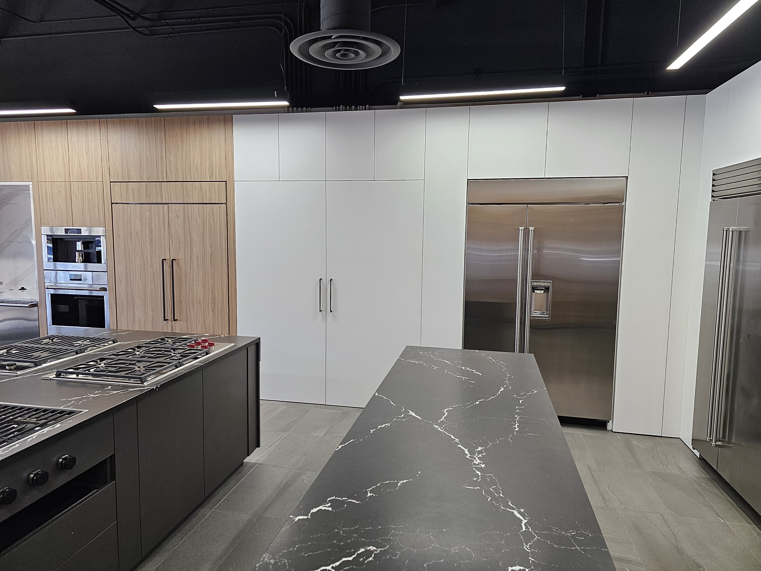 Modern kitchen with black, white, and wood cabinets, stainless steel appliances, and a dark marble countertop with white veins.