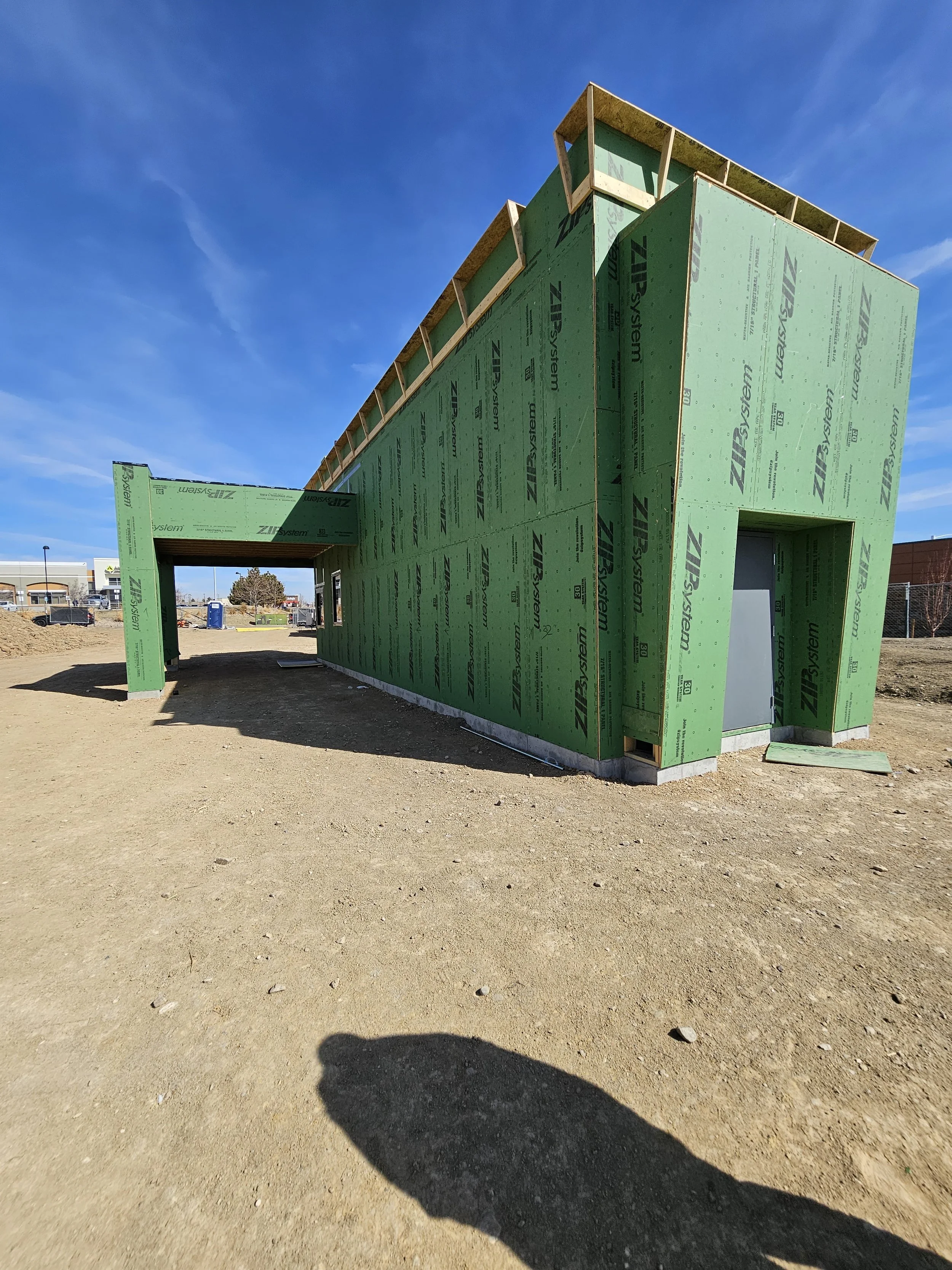 Building under construction covered in green sheathing with a blue sky background.