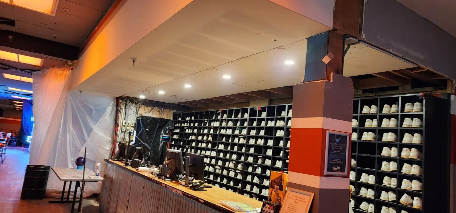 Shoe rental counter with a large wall of white shoes behind it, and computer stations on the counter in an indoor shopping or entertainment complex.