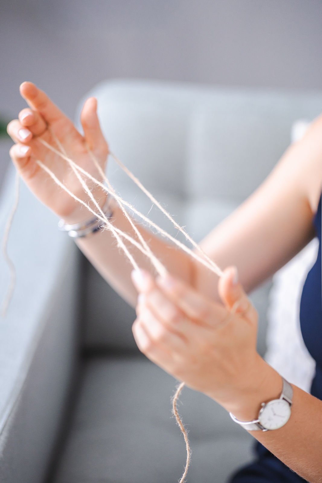 Nahaufnahme eines Armes, an dem ein Handgelenk mit einer Armbanduhr getragen wird, beim Stricken mit hellen Garnfasern.