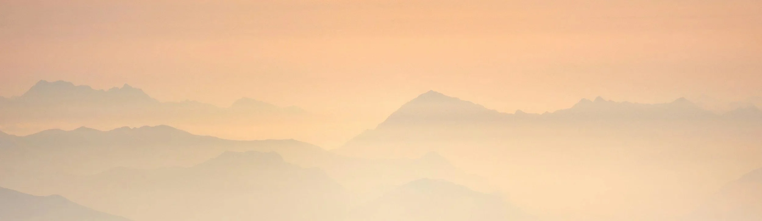 A pinkish-orange sky over a range of mountains with hazy, layered silhouettes.