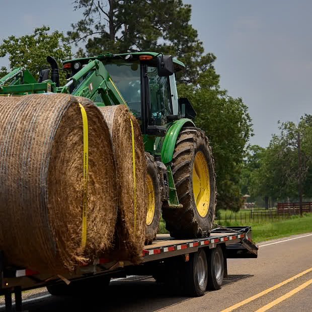 Agricultural equipment hauling in California using a flatbed trailer, transporting a tractor and hay equipment safely and securely.