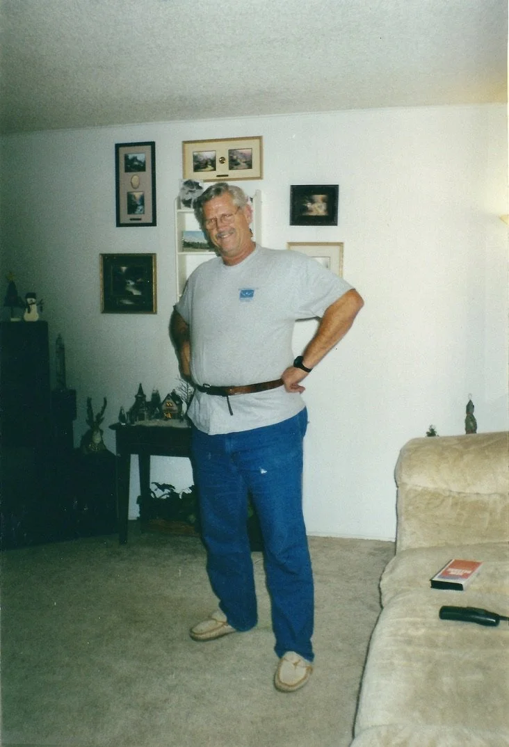 Andrew’s grandfather wearing glasses, a light gray T-shirt, and blue jeans, standing in a living room.