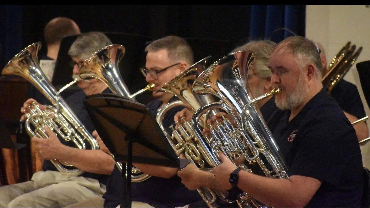 Group of musicians playing baritone saxophones at a concert, reading sheet music.