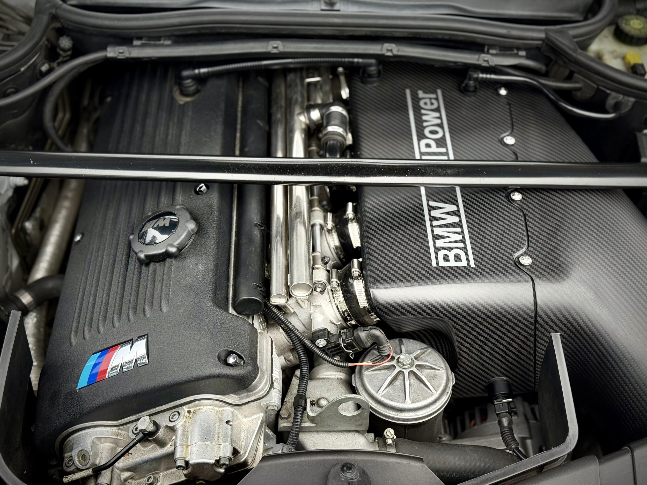 Close-up of a BMW engine with an M Power badge, showing various metallic engine components and hoses.