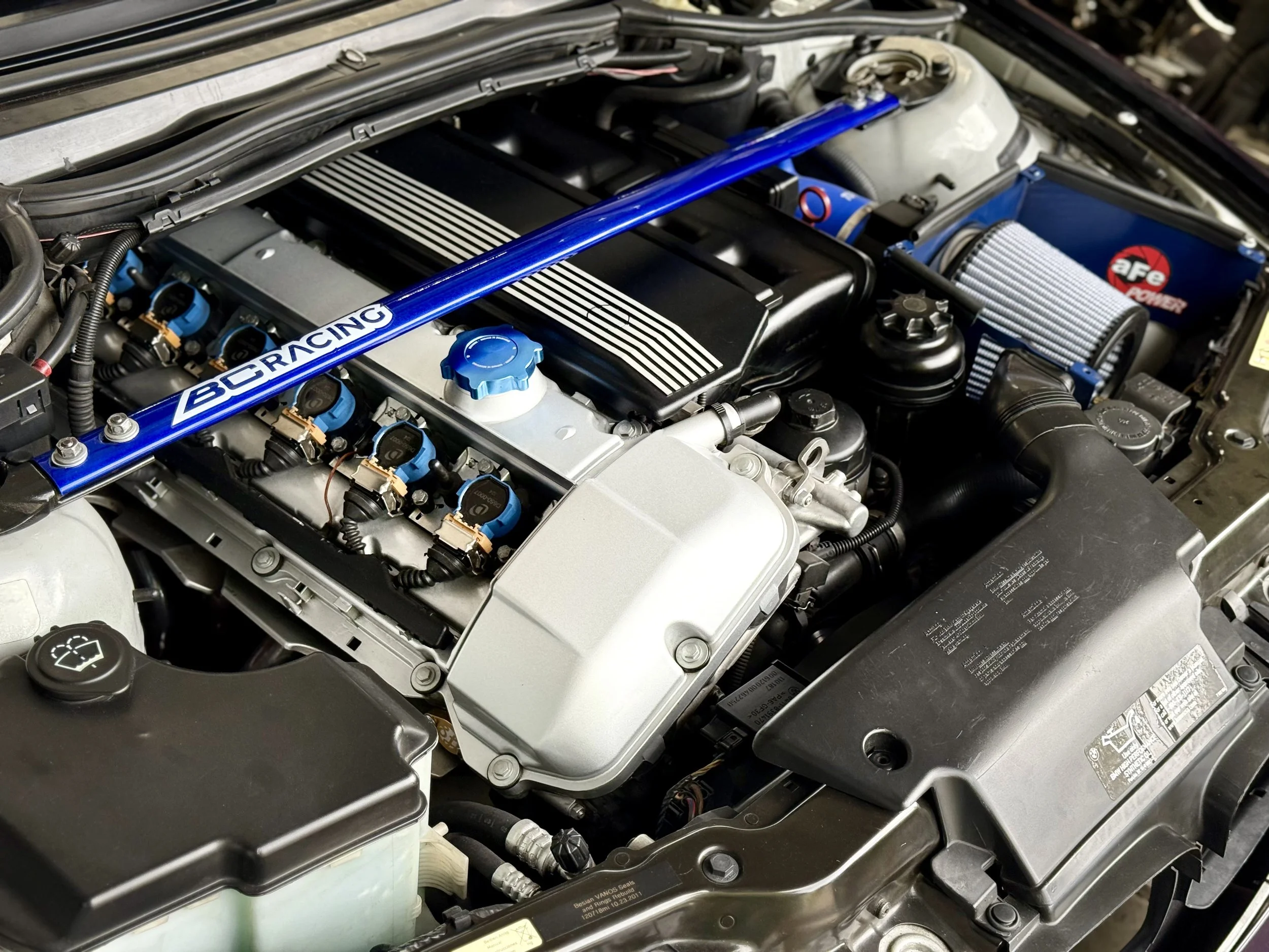 Close-up of a car engine with a blue sway bar labeled BC RACING, an aftermarket cold air intake, and various engine components.