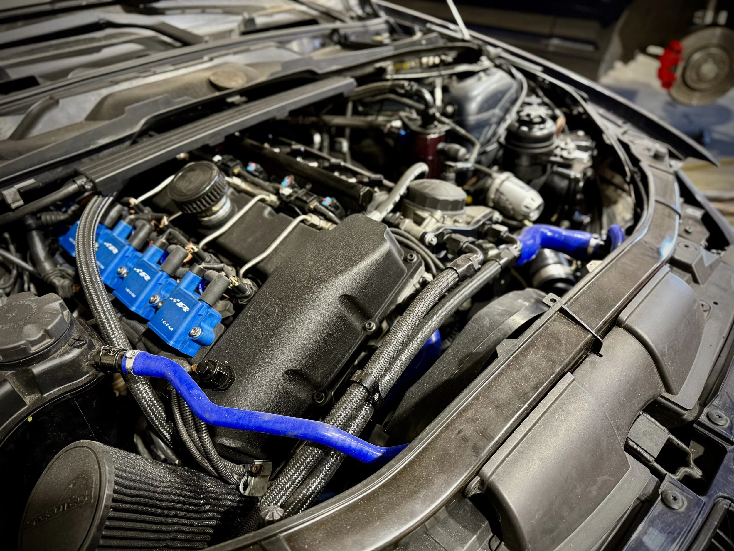 Close-up of a car engine with various hoses and components, including blue accents.