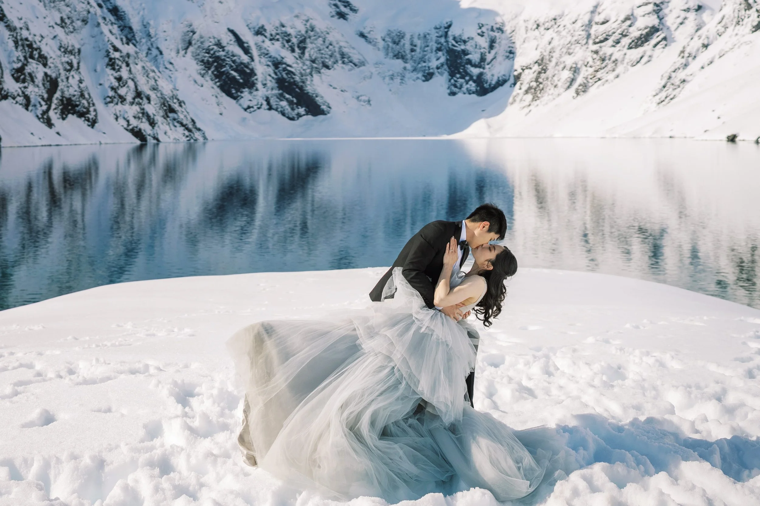 Newlywed couple kissing in the snow beside Lake Erskine
