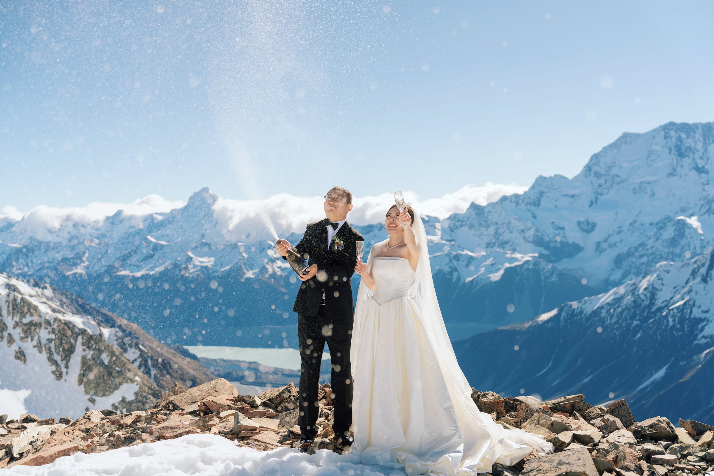 Bride and groom celebrating with champagne on a snowy mountain summit at Mount Cook