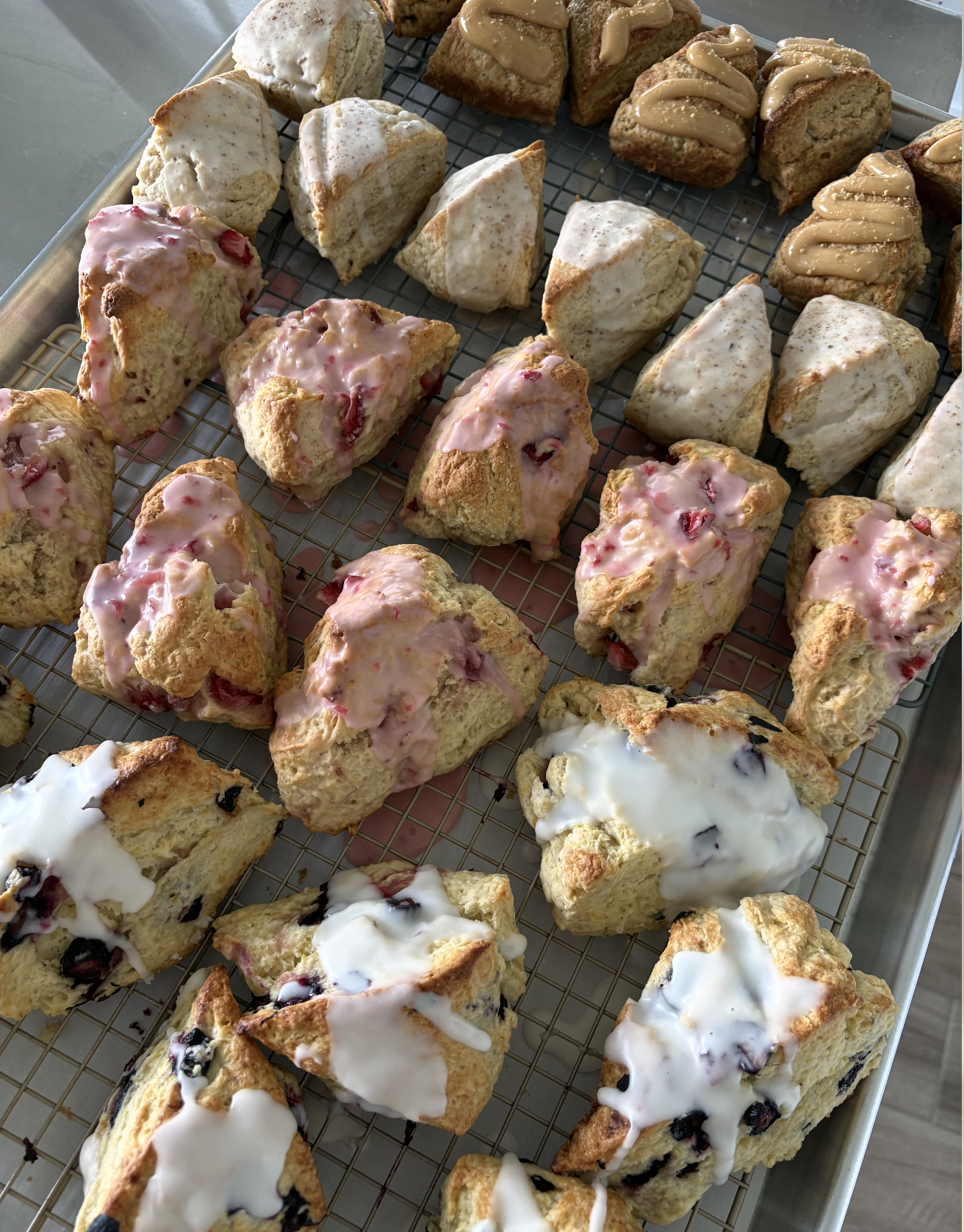 Assorted scones topped with glaze and icing, arranged on a wire rack.