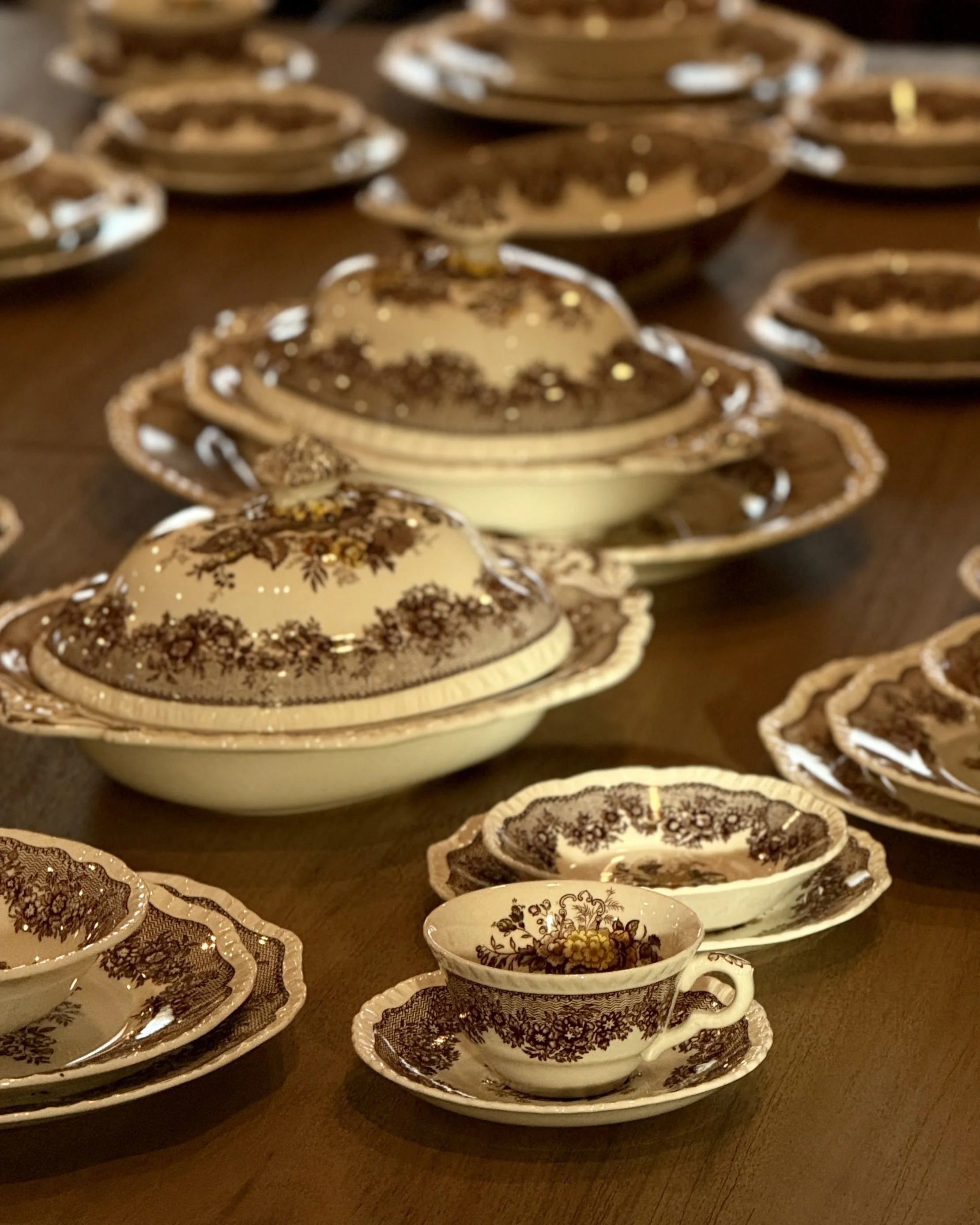 Multiple vintage tea cups and saucers with floral and decorative patterns arranged on a wooden table.