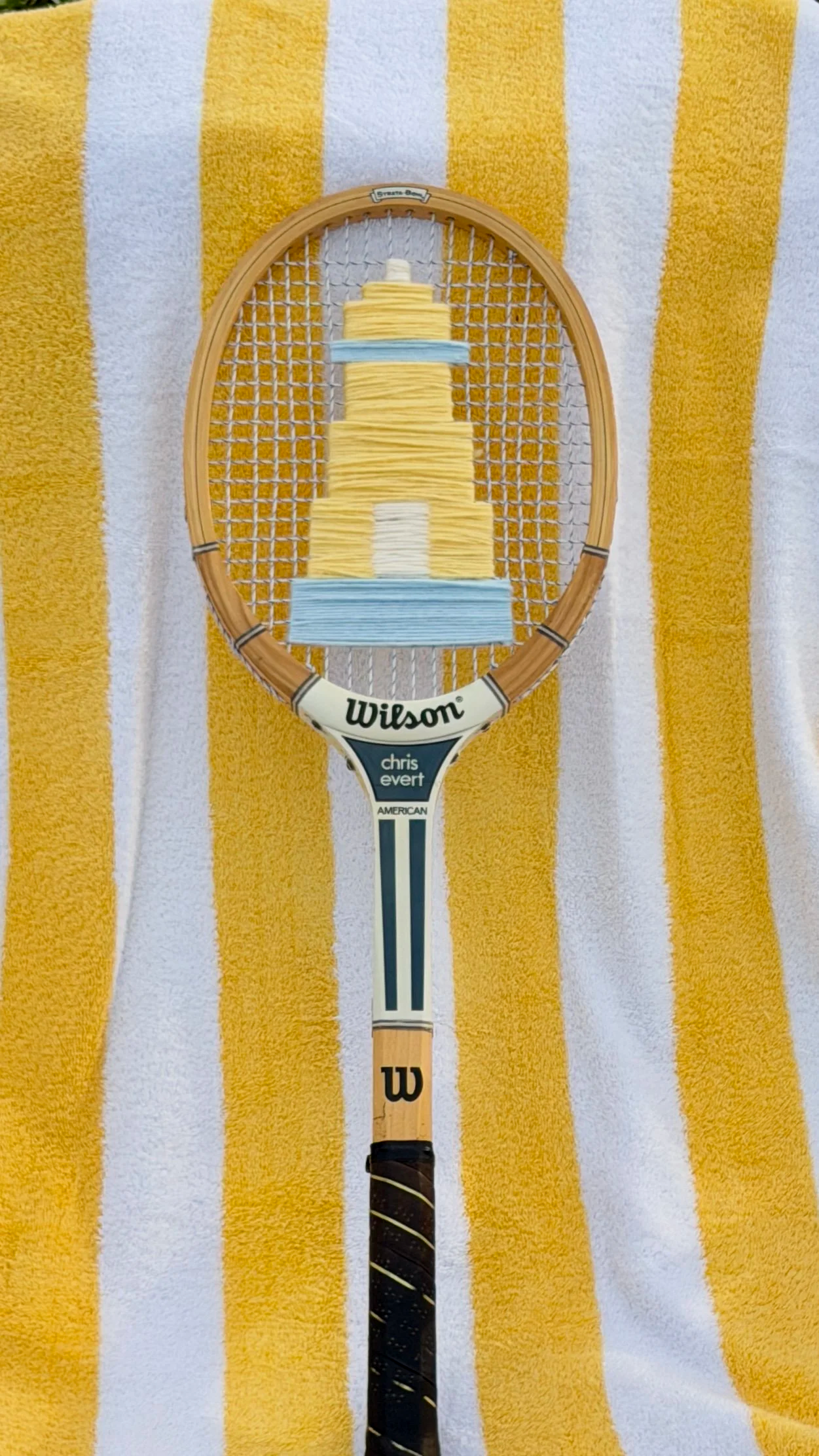 A tennis racket with a string pattern designed to resemble a multi-tiered cake on a yellow and white striped towel.