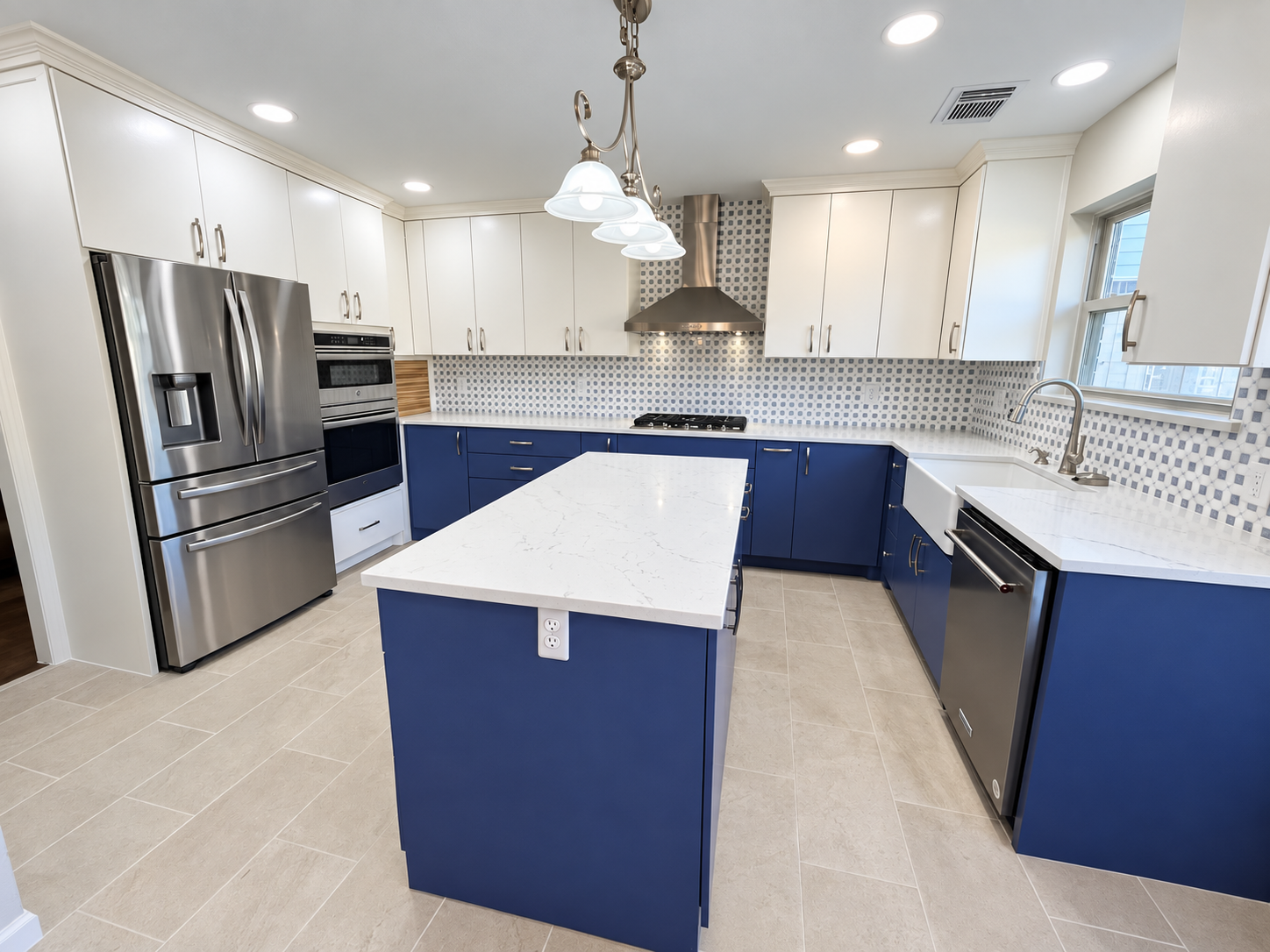 Modern kitchen with white upper cabinets, blue lower cabinets, stainless steel appliances, a white marble island, and a patterned backsplash.