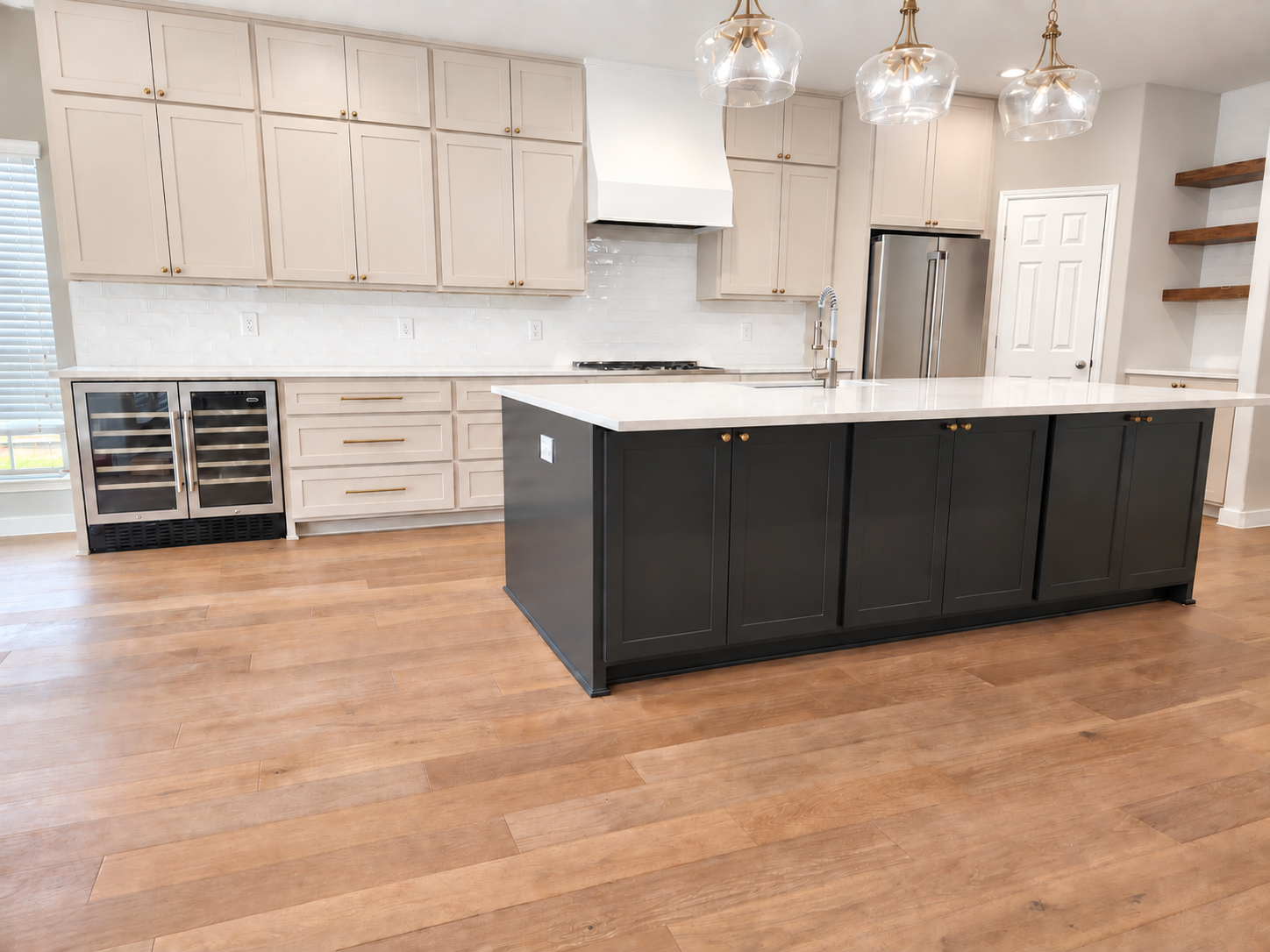Modern kitchen with white upper cabinets, black island, wood flooring, stainless steel appliances, and pendant lighting.