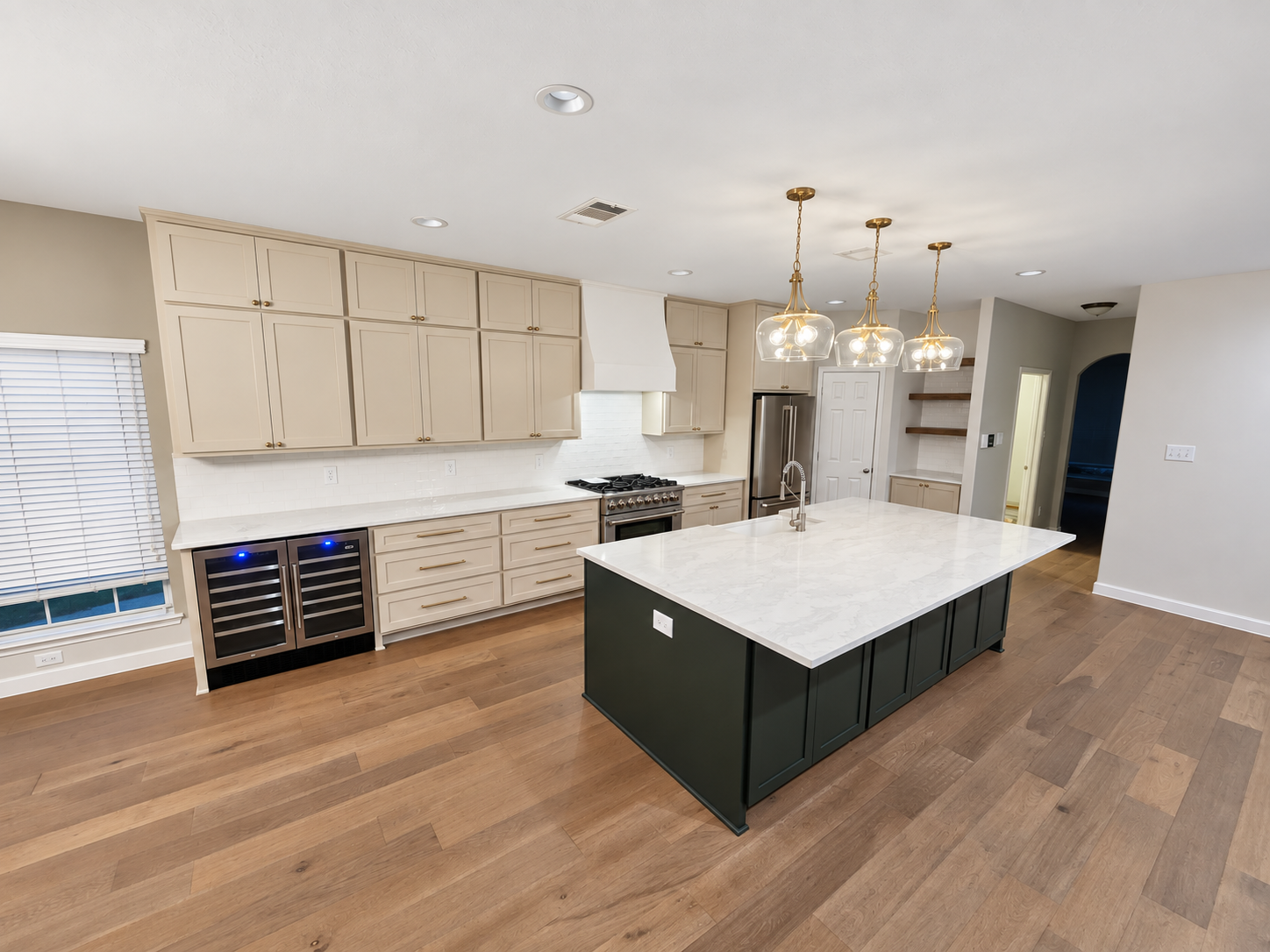 Modern kitchen with beige cabinets, a marble island with dark green base, stainless steel appliances, hardwood floors, and pendant lighting.