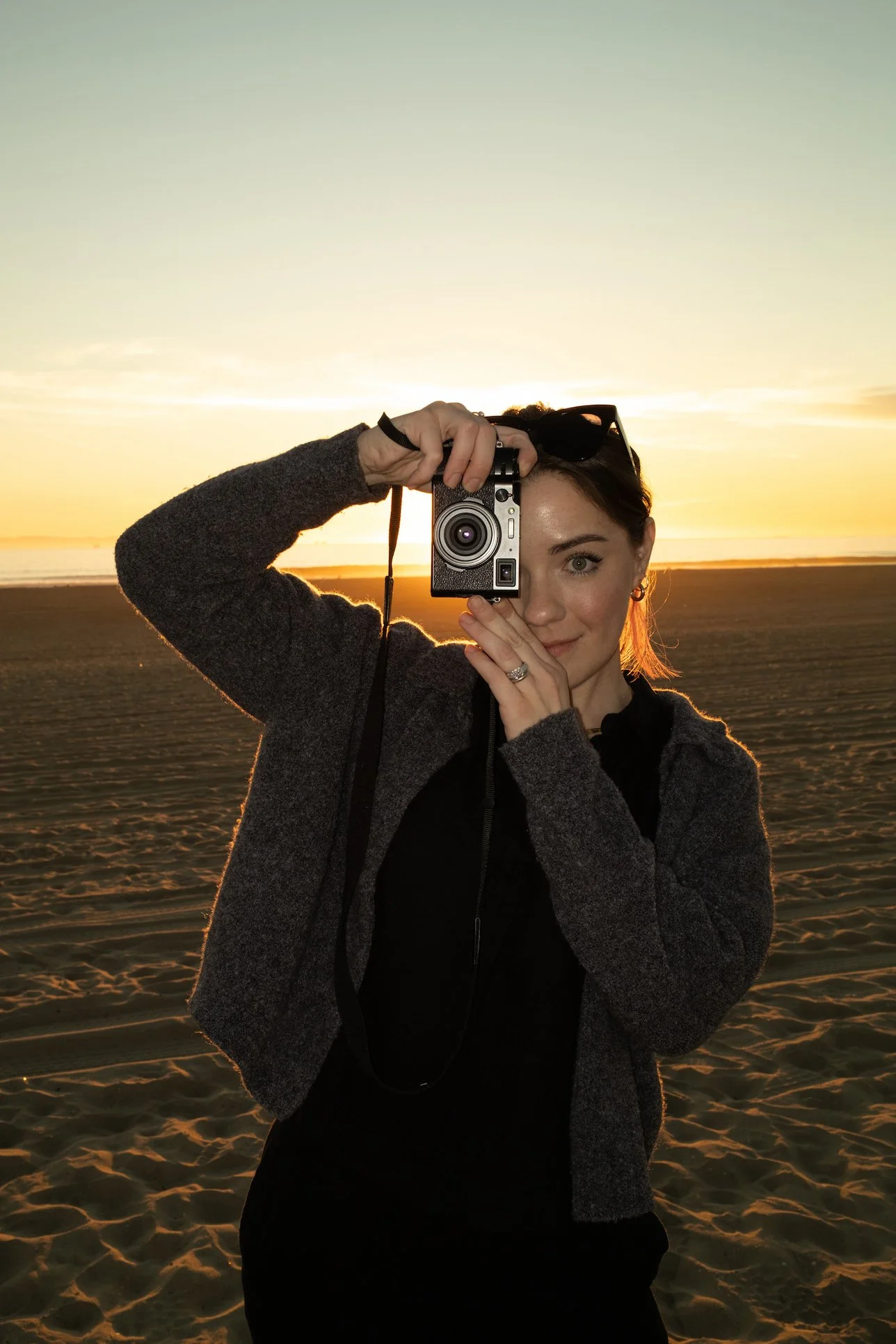 Margaret, Kiss Kiss founder and wedding content creator, holding a camera up to her eye on the beach at golden hour.