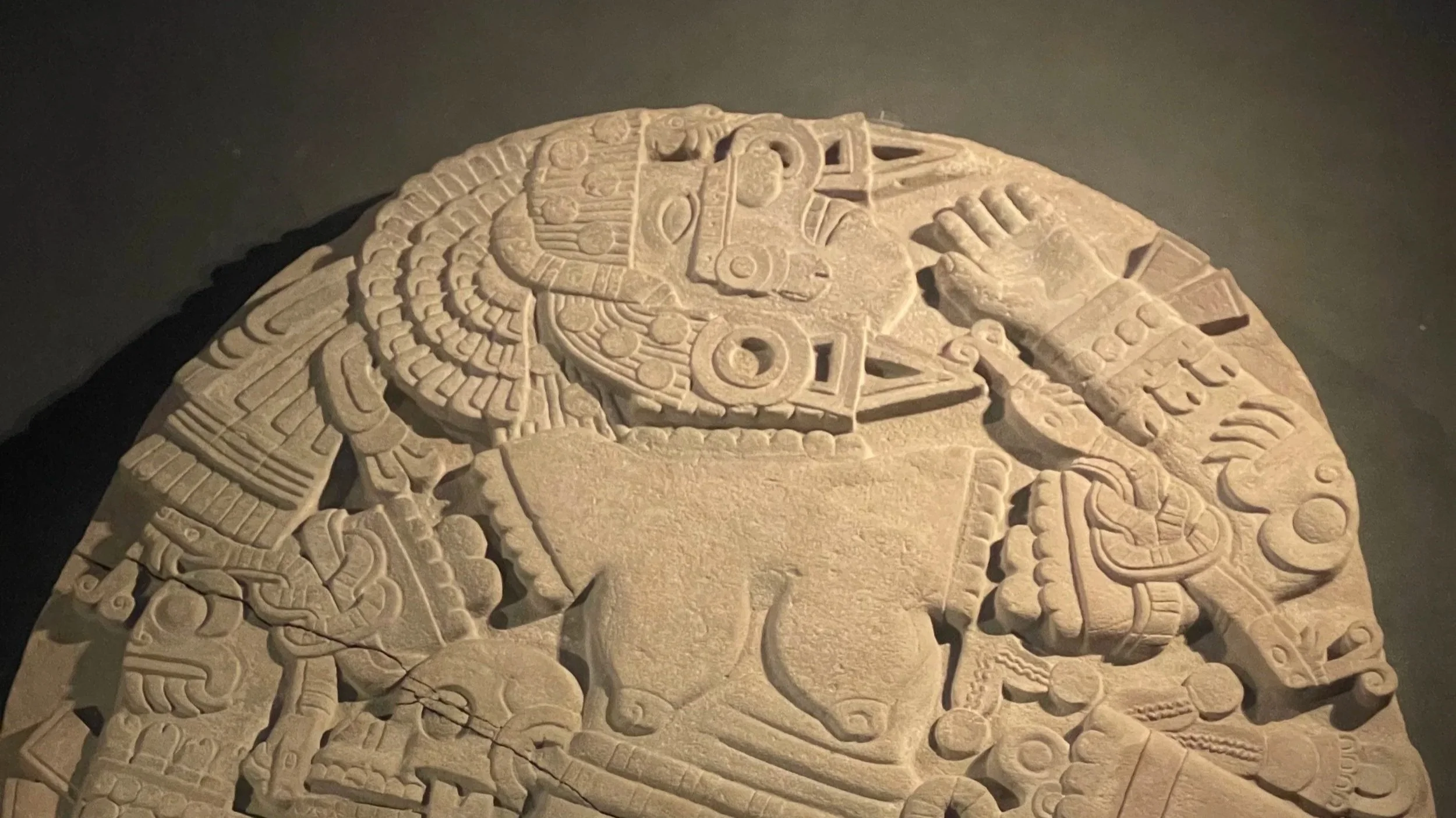 An ancient carved stone featuring intricate Mayan glyphs and depictions of a figure wearing elaborate headdress and jewelry.