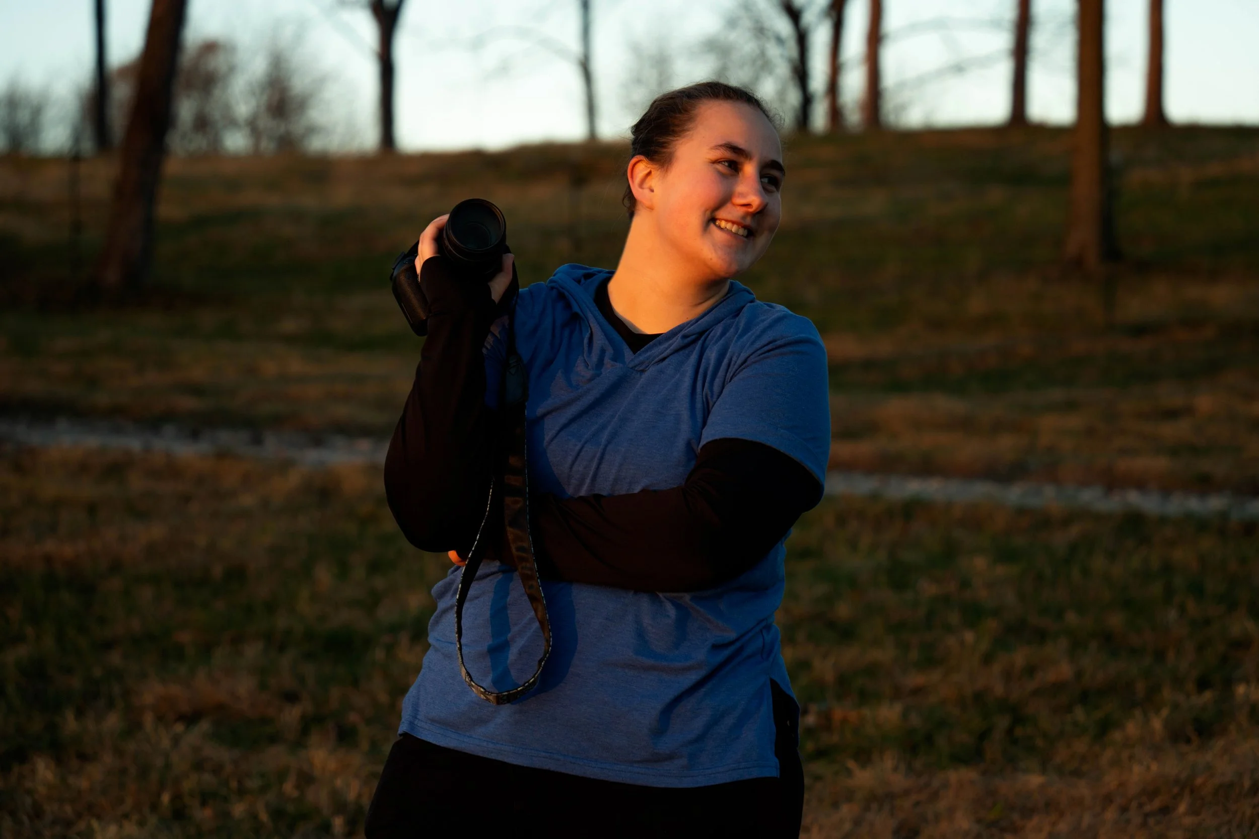 Parren smiling outdoors while holding her camera at golden hour.