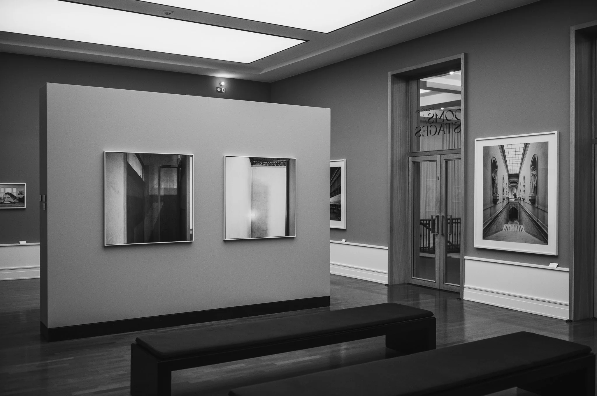 Black-and-white photograph of a gallery room at the Museum für Fotografie in Berlin, framed photographs on a free-standing wall above dark benches