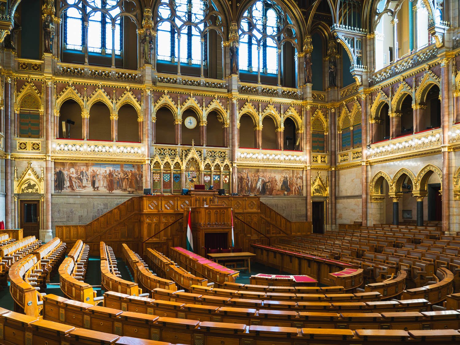 Debating chamber inside the Hungarian Parliament Building, curved rows of wooden benches below gilded Gothic arches and tall windows