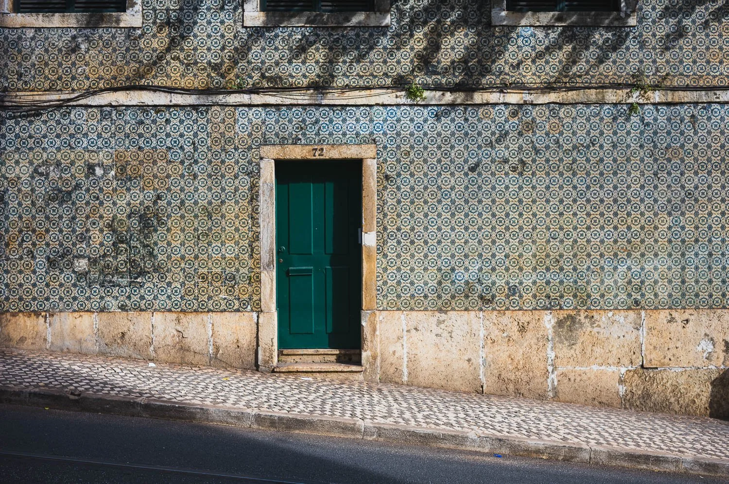 Wall of patterned blue azulejo tiles around a single green door on a sloping Lisbon street