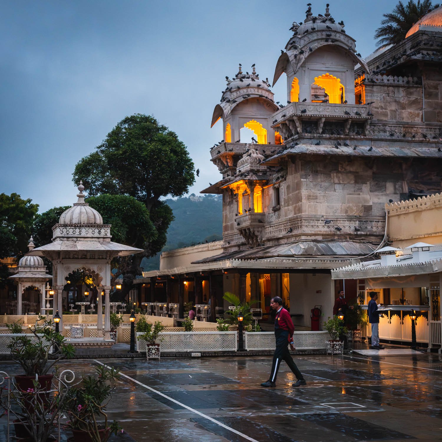 Jag Mandir's lit pavilions at dusk, a figure crossing the wet courtyard