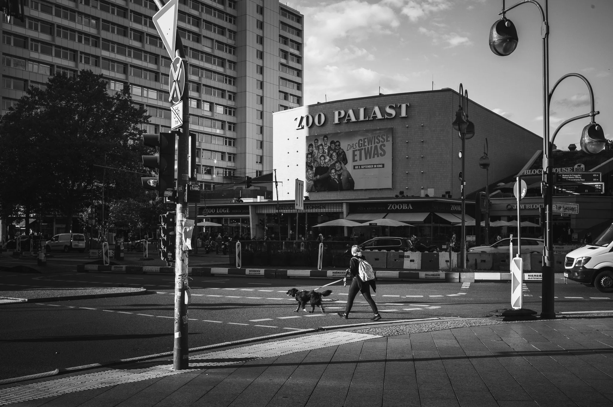 Black-and-white photograph of a woman walking her dog across a road junction in front of the Zoo Palast cinema in Berlin