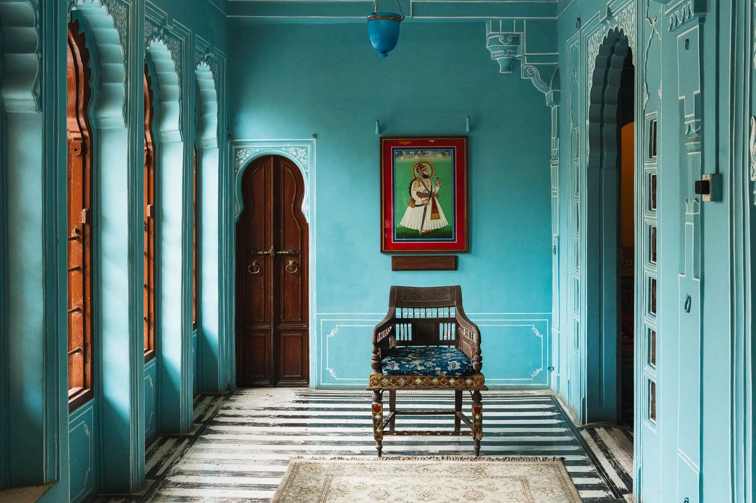 A turquoise palace room with a carved chair beneath a framed portrait