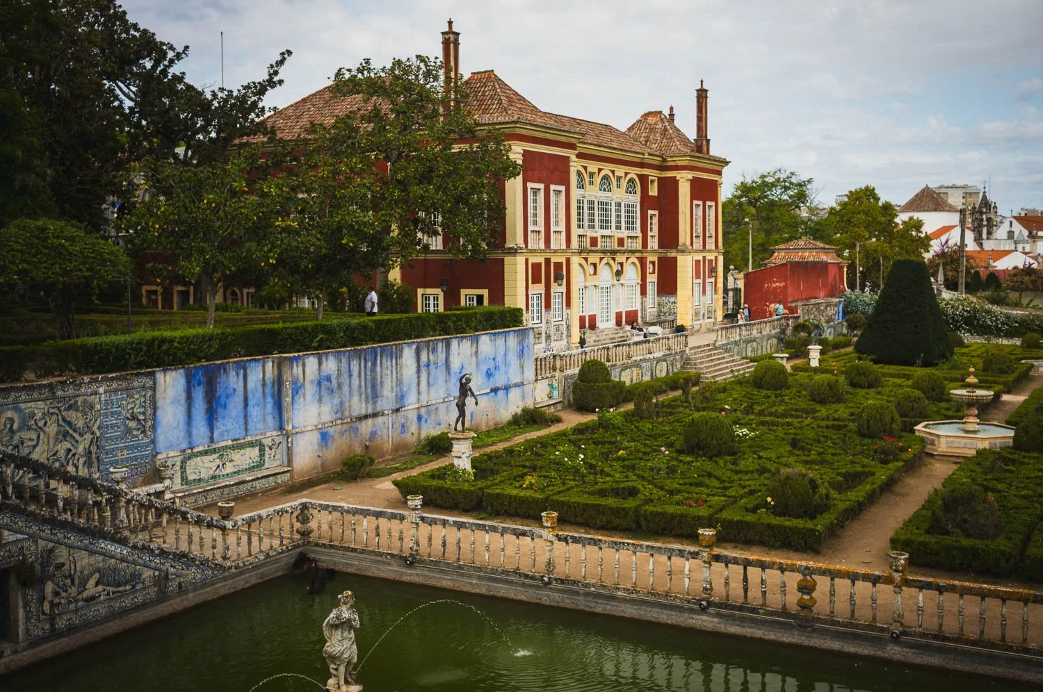 Formal garden with box hedges and a pond lined with blue azulejos, a red palace beyond