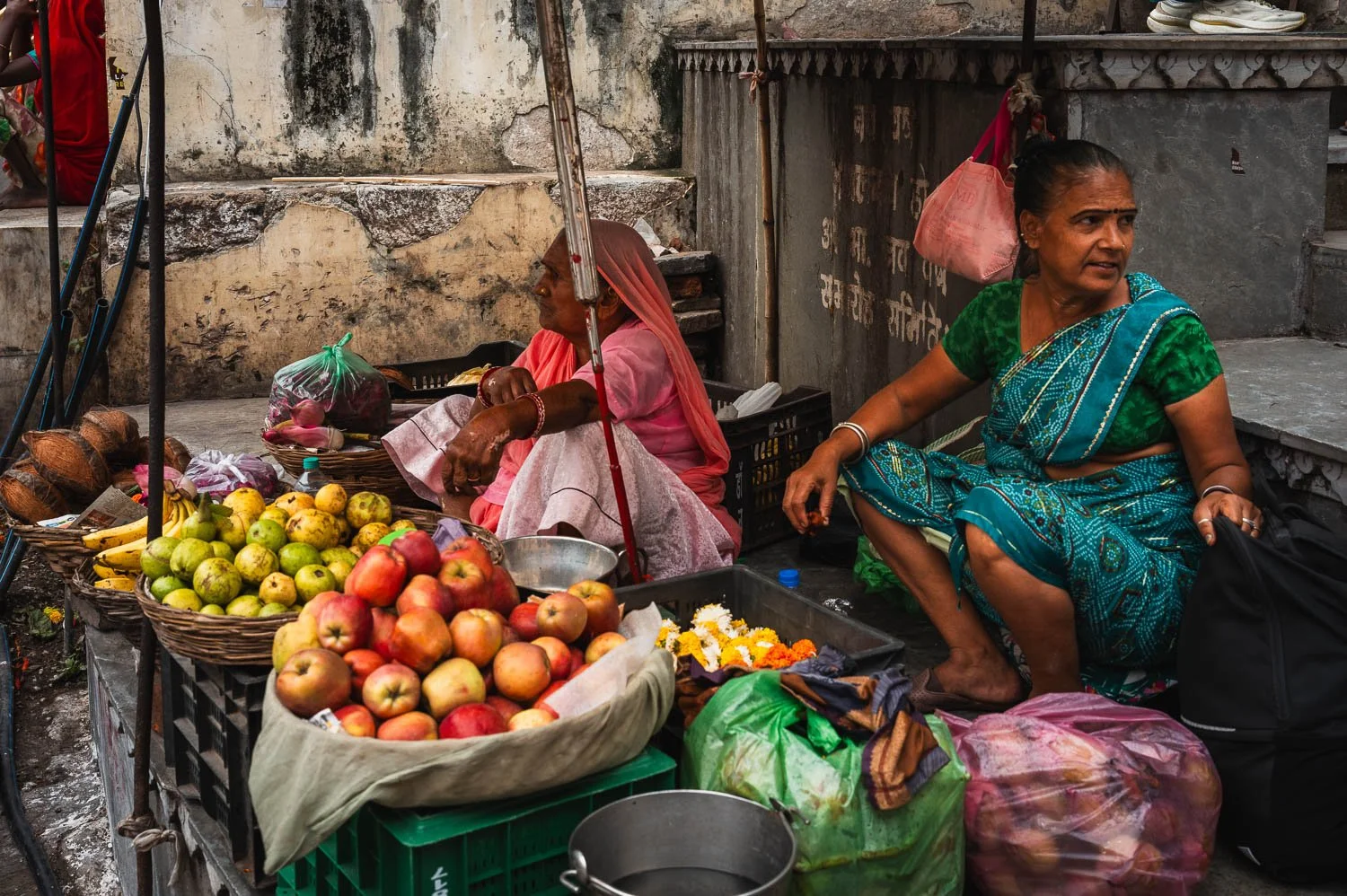 A woman in a green sari sells apples and fruit from baskets on a street corner