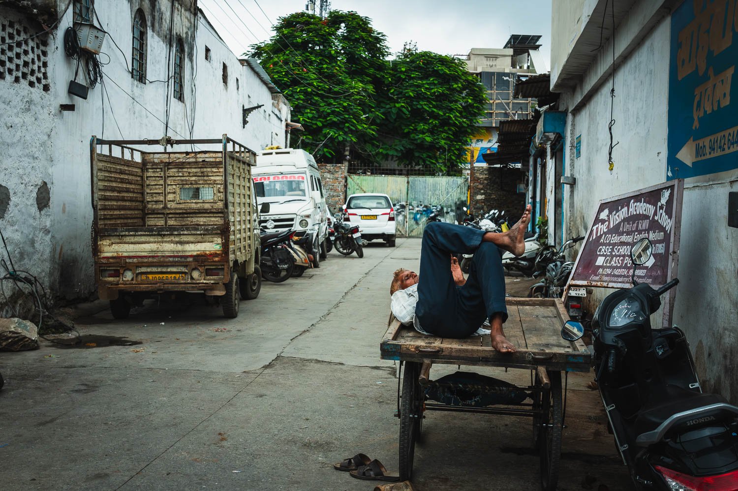 A man asleep on a handcart in a narrow lane