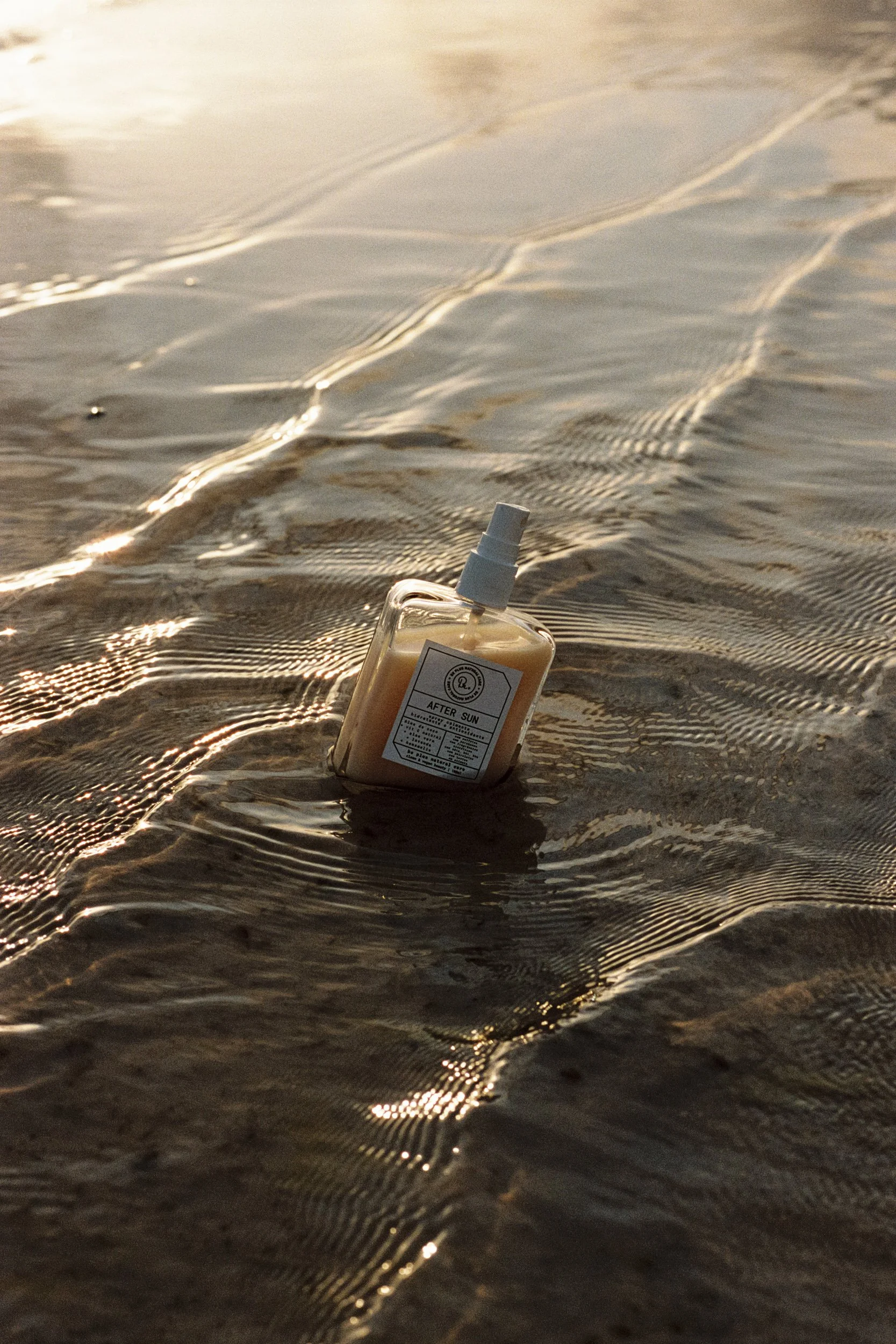 Product bottle resting in shallow lagoon water at sunset, 35mm film