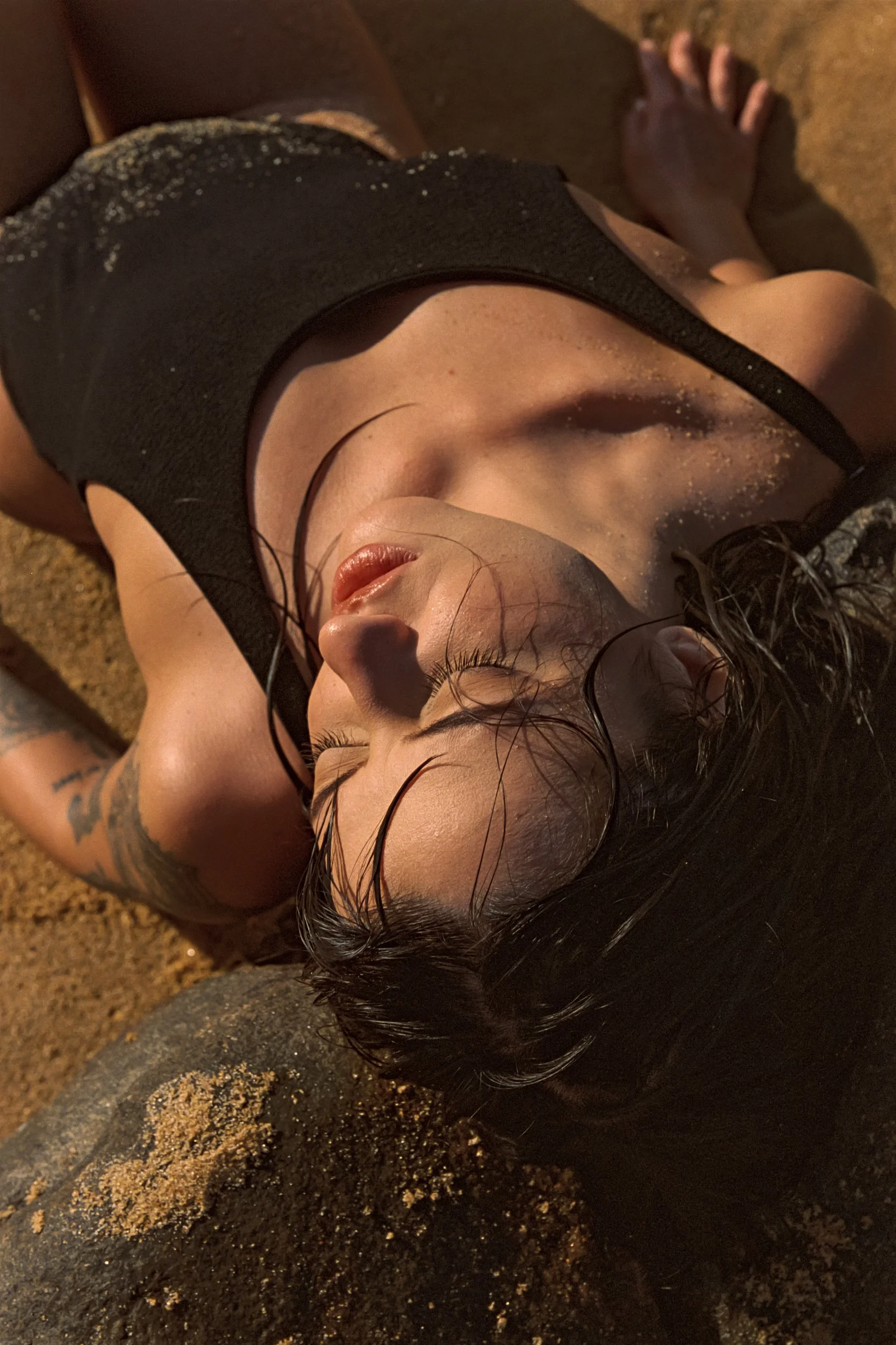 Overhead frame lying back on sand, eyes closed, wet hair, 35mm film