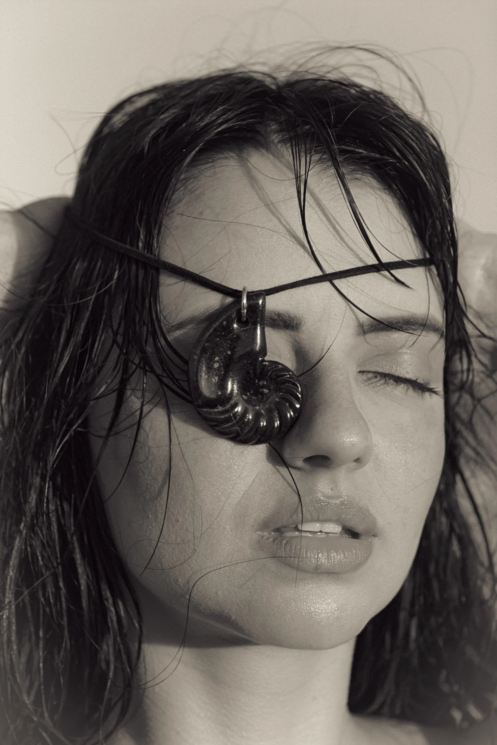 Head tilted back, shell pendant covering one eye, black and white, 35mm film