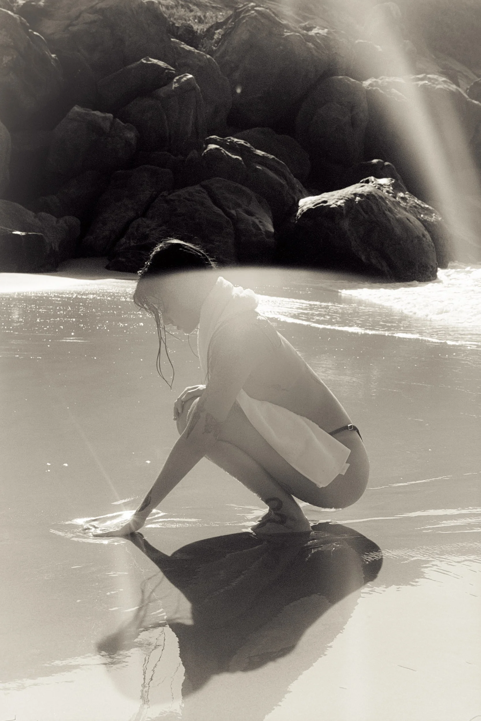Crouching at the water's edge in a white shirt, black and white, 35mm film