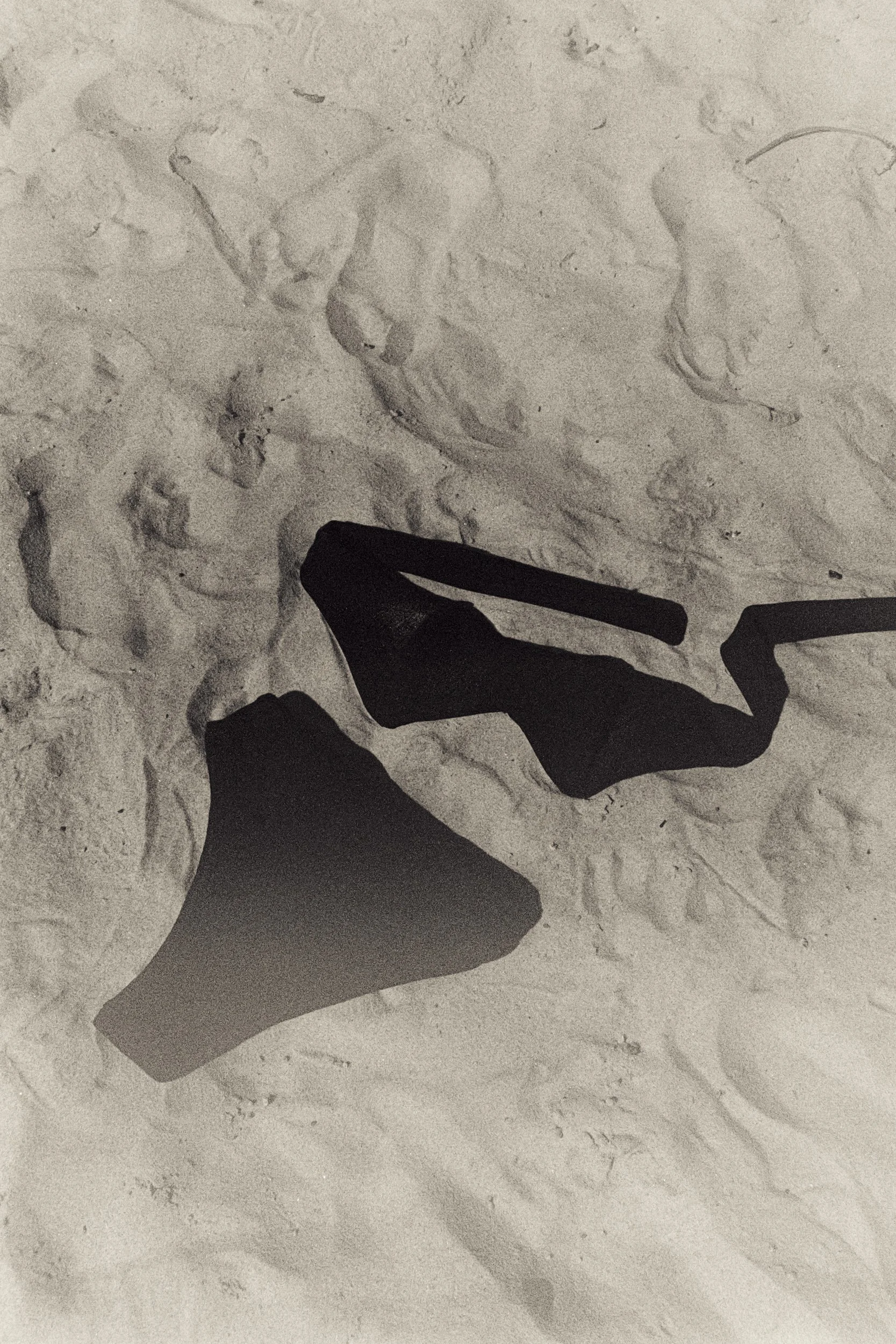 Clio black bikini laid on sand among footprints, 35mm film