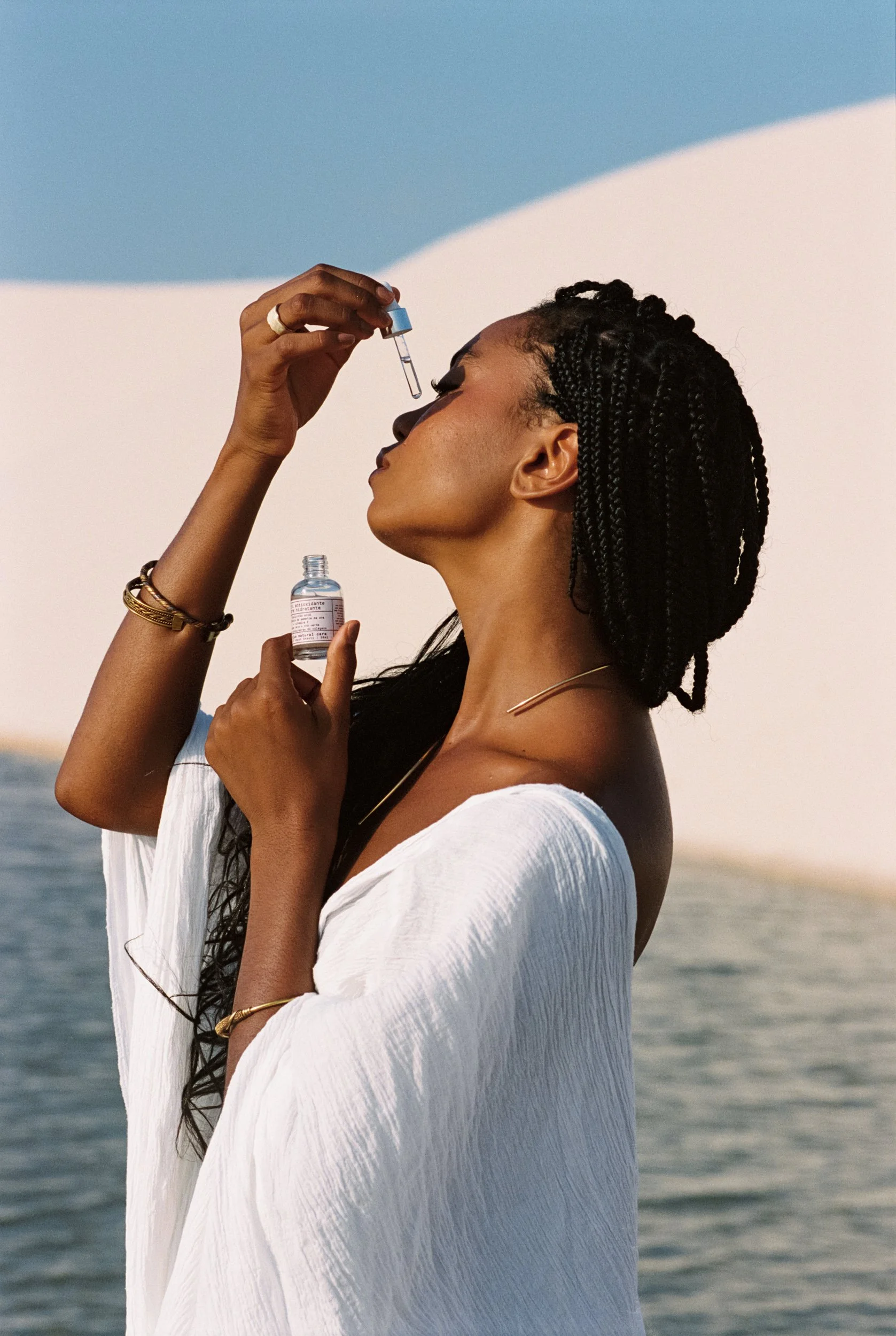 Model applying Be Plus serum, white dunes and blue sky, Lençóis Maranhenses, 35mm film