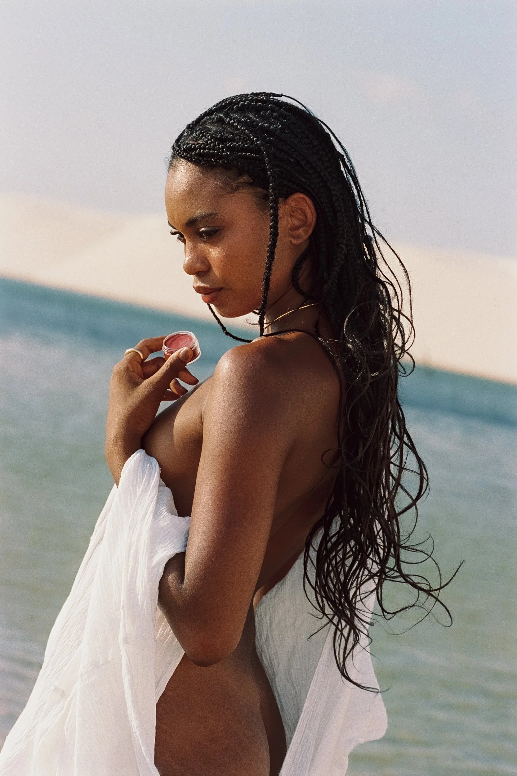 Model opening Be Plus balm jar, dunes and lagoon behind, Lençóis Maranhenses, 35mm film

Model draped in white cotton dipping a finger into a balm jar by the lagoon, Be Plus Natural Care, Lençóis Maranhenses, Brazil.