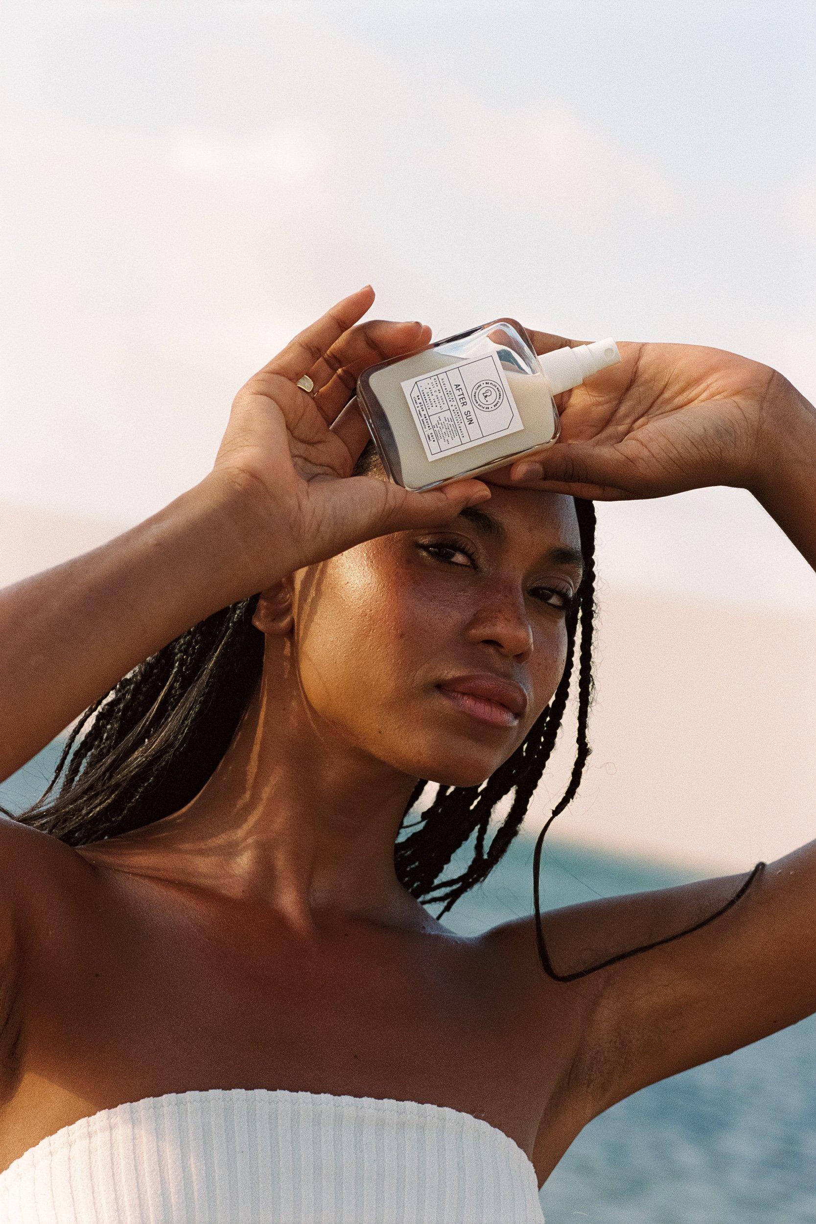 Model holding an After Sun product bottle sideways above her brow with both hands, Be Plus Natural Care, Lençóis Maranhenses, Brazil, on 35mm film.