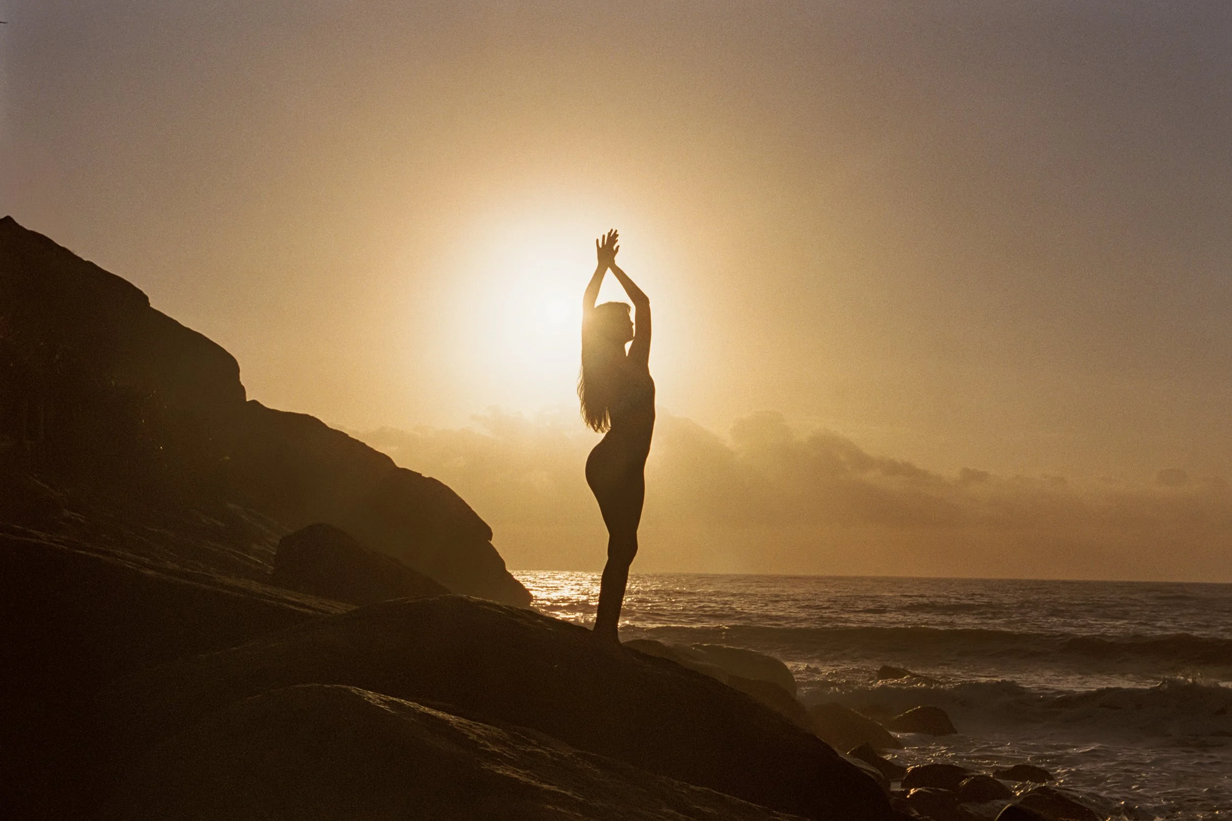 Arms stretched overhead in silhouette on the rocks at sunset, 35mm film