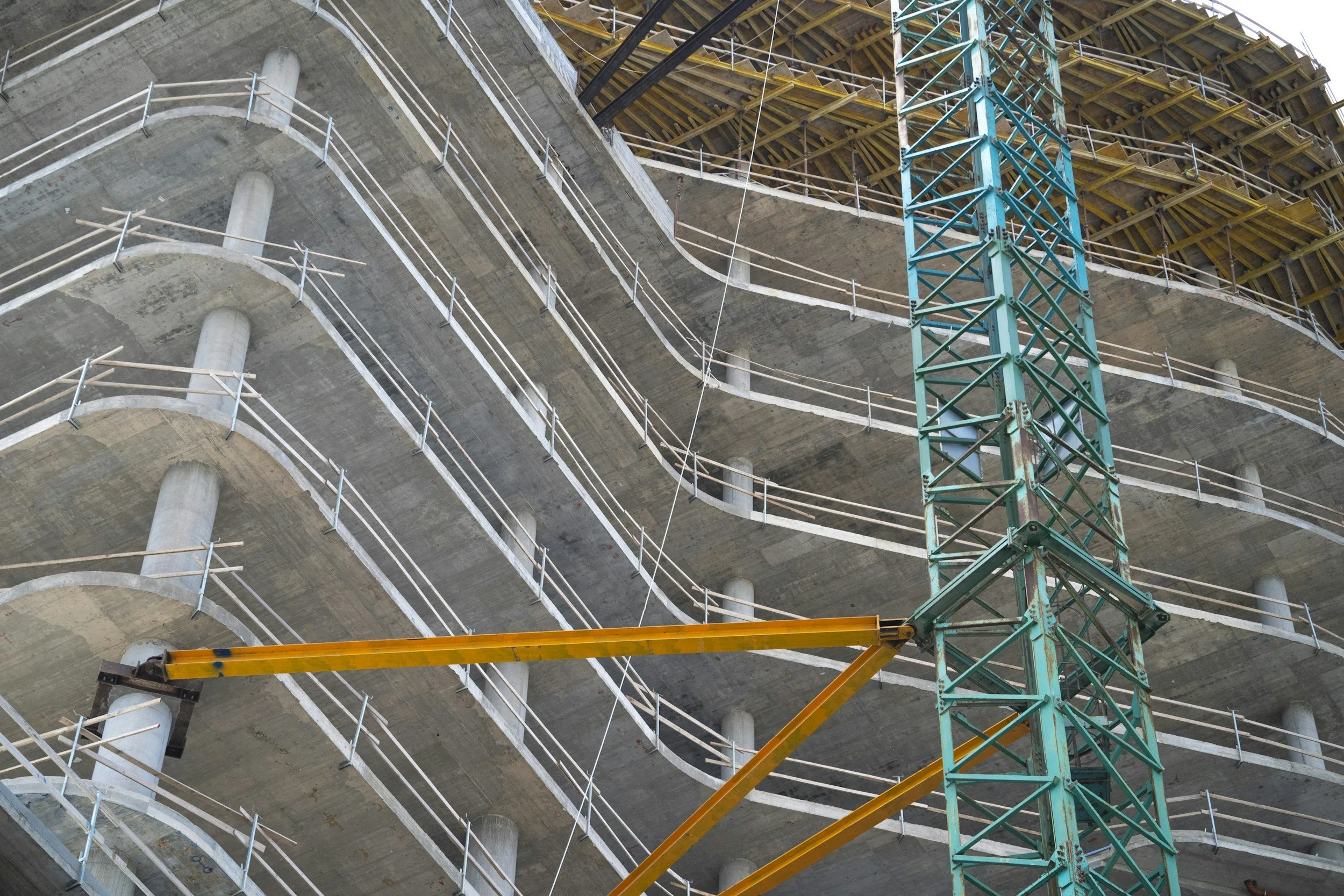 A multi-story building under construction with concrete floors, temporary safety railings, and a green construction crane.