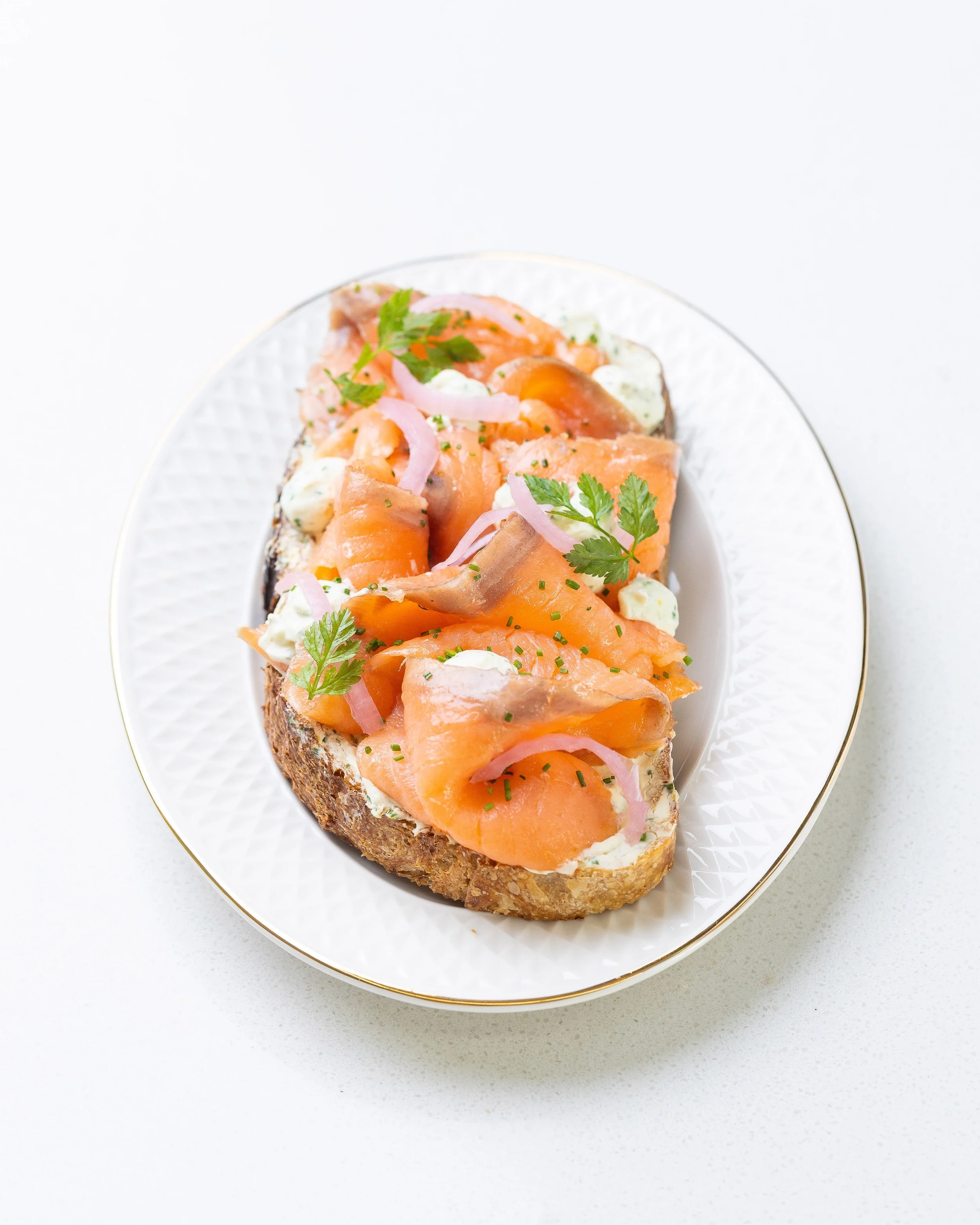 Close-up of smoked salmon canapé on a white plate, garnished with herbs, onions, and a creamy sauce.