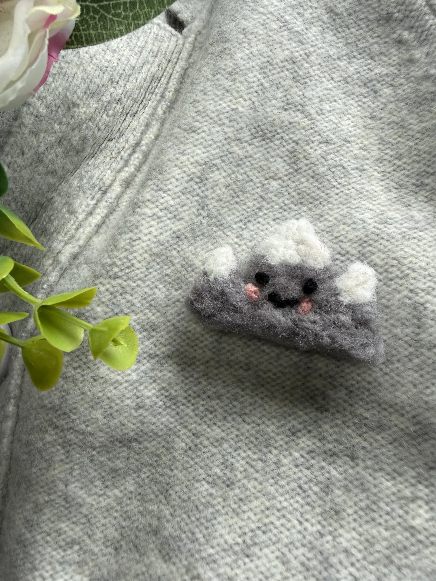 Close-up of a small felted mountain pin with pink nose and black eyes.