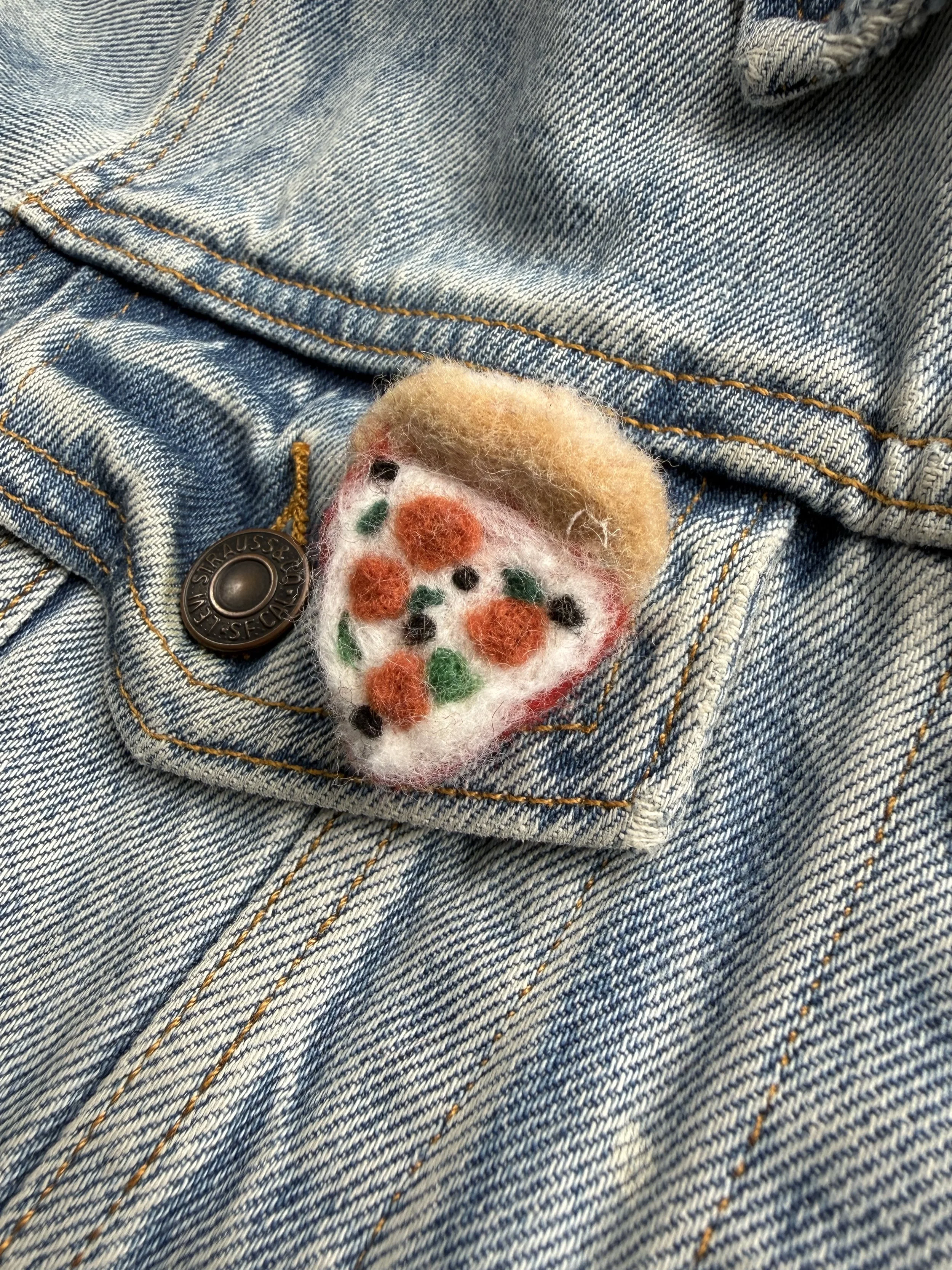 Close-up of a denim jacket pocket with a felted pizza pin.