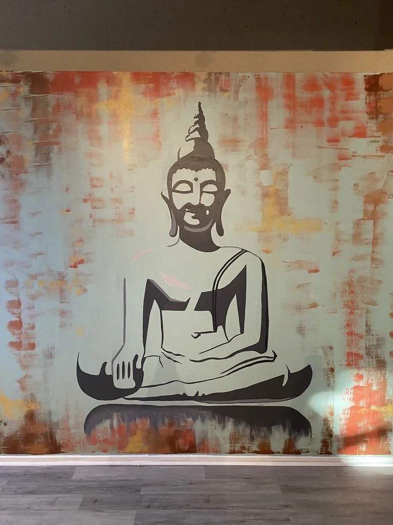 Wall mural of a black and white outline of Buddha sitting cross-legged, with a background of warm, abstract brushstrokes in red, orange, and yellow hues.