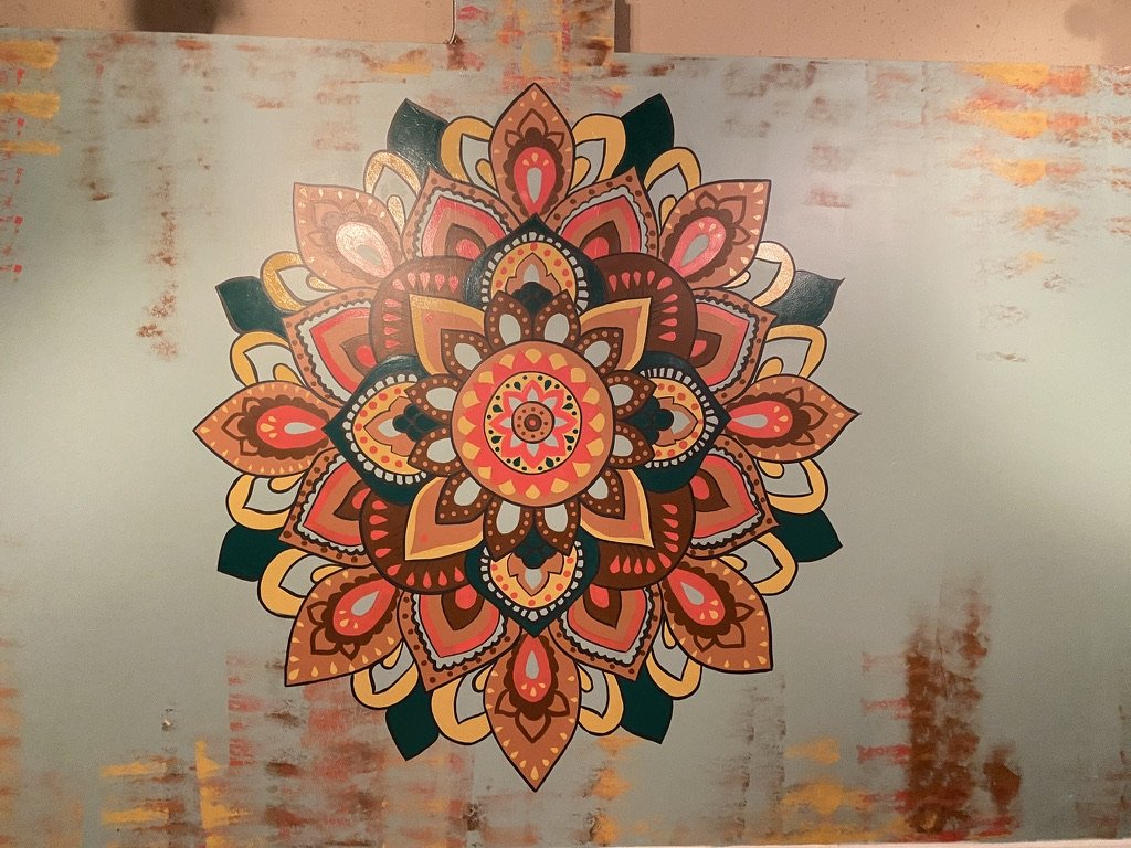 Colorful mandala with intricate patterns and floral shapes painted on a textured wall.