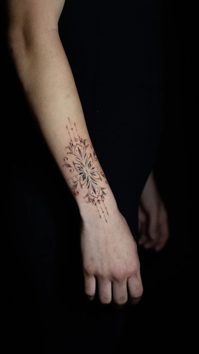A person's arm with a large, ornate tattoo of a butterfly surrounded by decorative swirls and patterns.